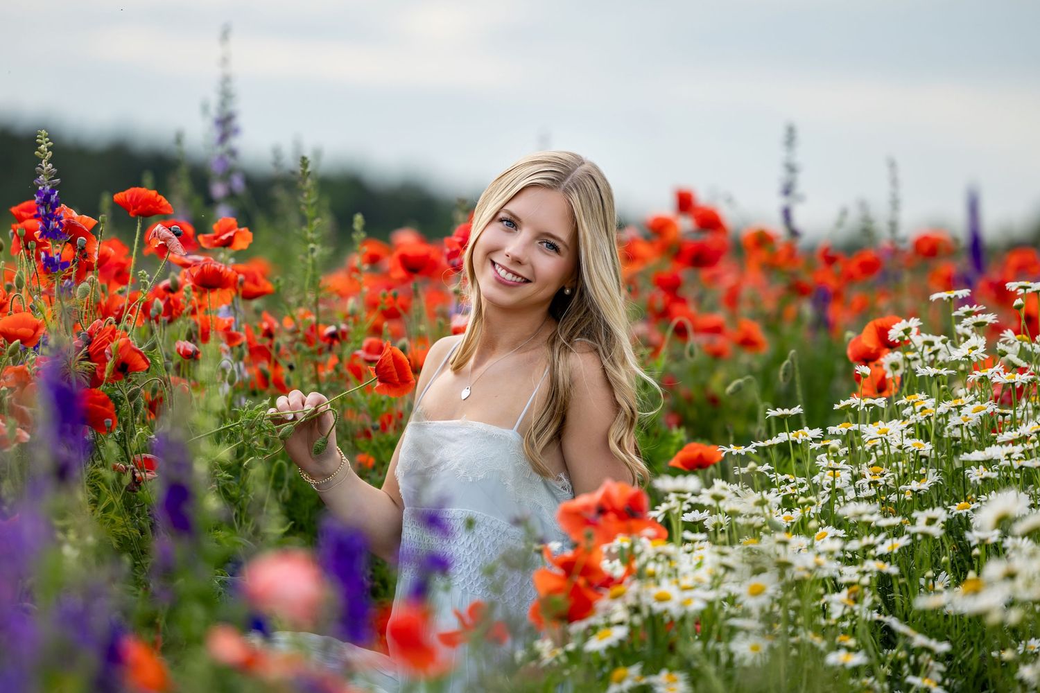 A woman stands joyfully in a vibrant field of red poppies and white daisies on a sunny summer day.