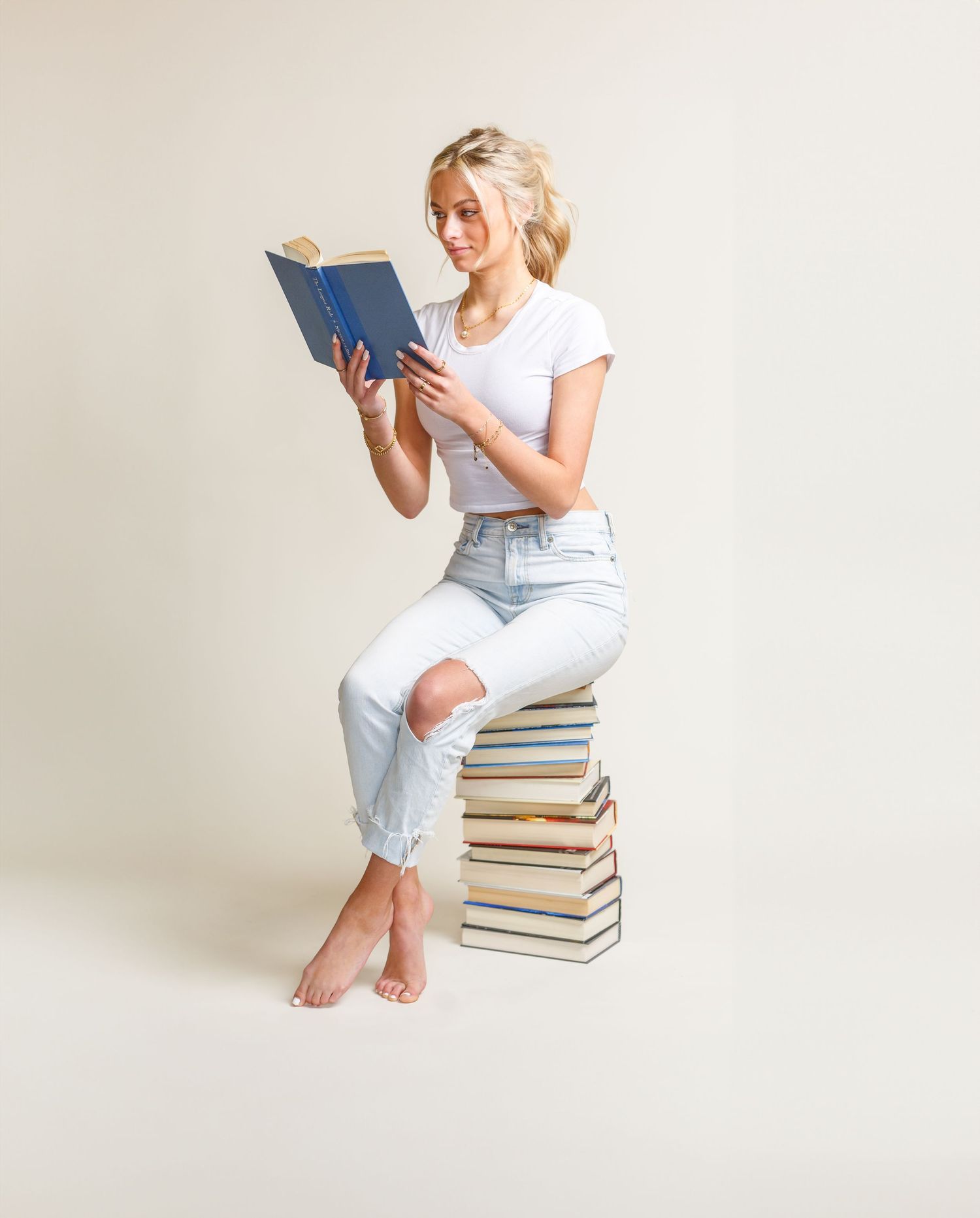 studio portrait of a girl reading a book. Creative image of a girl on a stack of books.