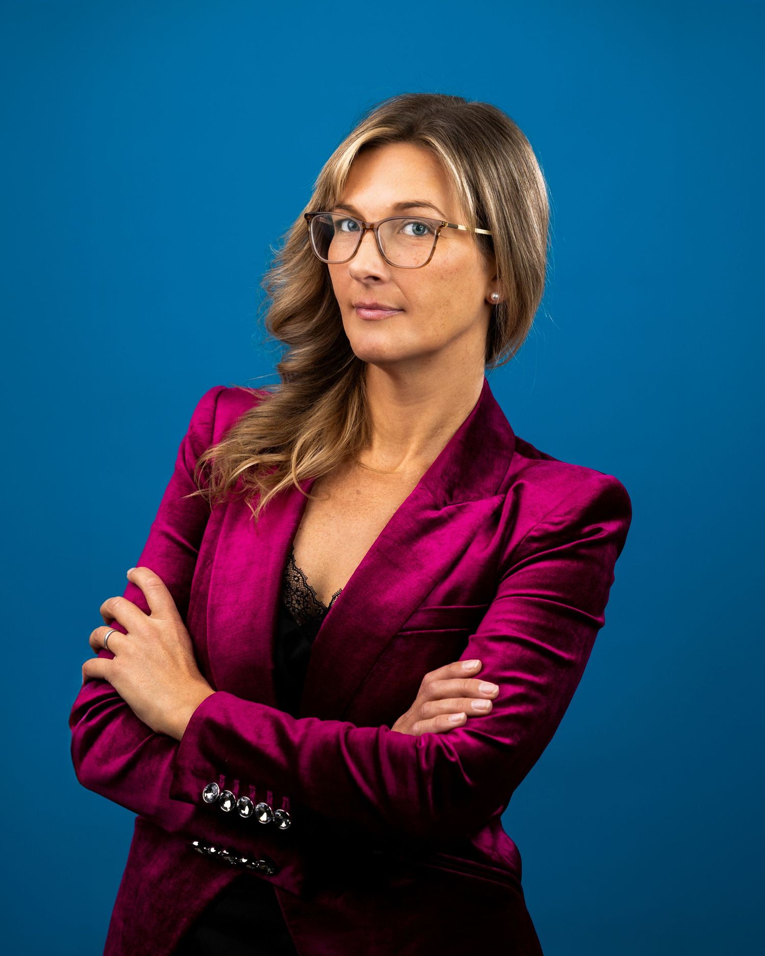 Professional portrait of someone in a magenta blazer and glasses posing confidently against a blue background.