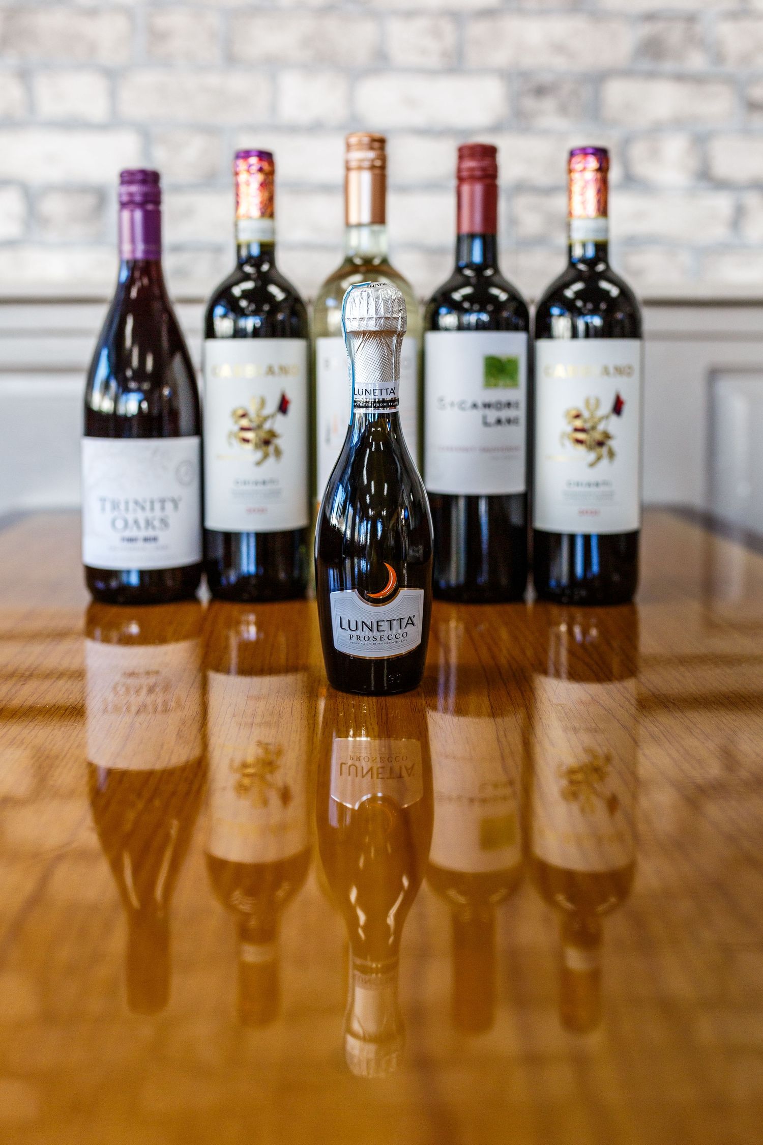 Collection of wine bottles arranged on wooden table with reflective surface against brick wall, featuring Pioneer brand.