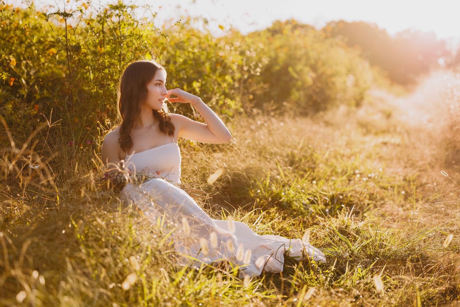 A silhouette sits in a sun-drenched meadow with tall grass and wildflowers during golden hour.