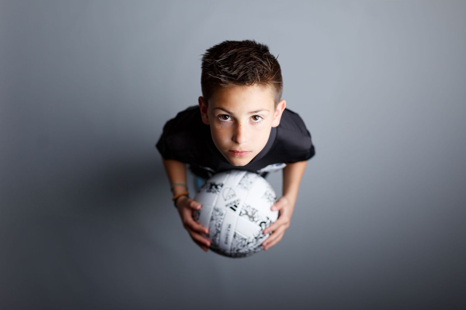An overhead view of a young soccer player holding a ball while wearing a black jersey.