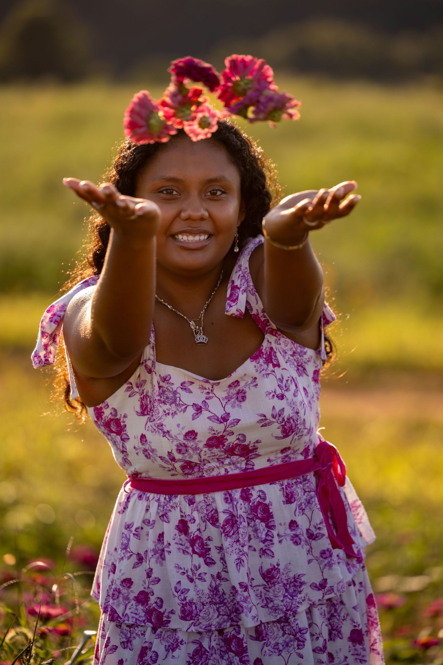 A person in a pink floral dress reaches out joyfully in a sunny outdoor setting with autumn leaves on the ground.