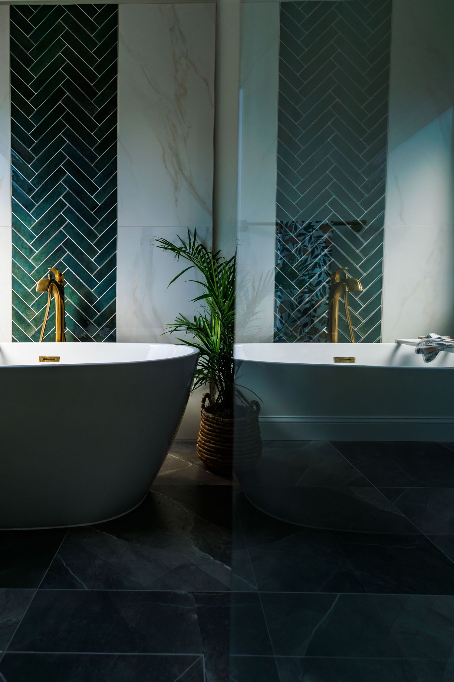 Modern bathroom interior with dark chevron tiles and freestanding bathtub next to a potted palm.