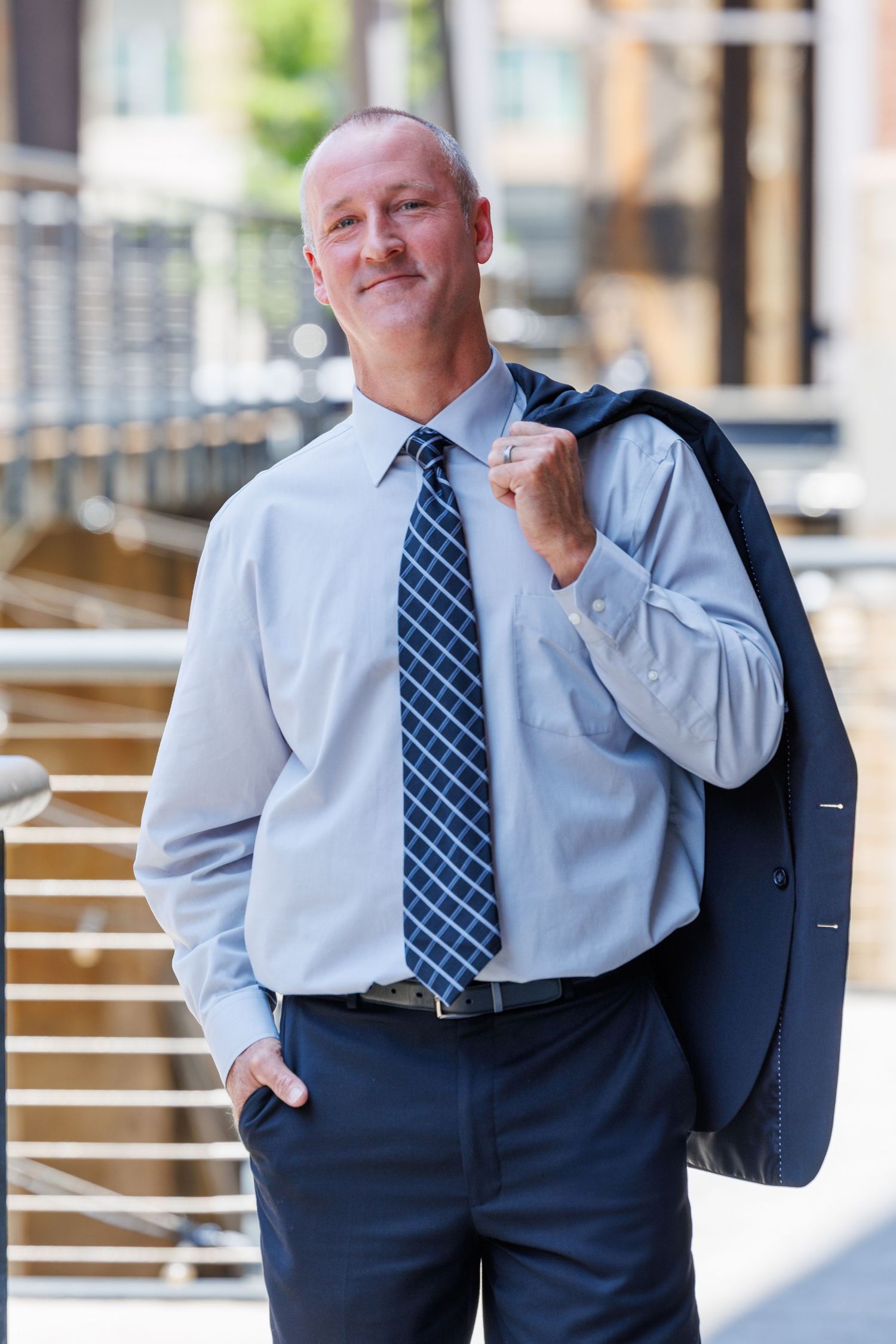 Professional in business attire stands confidently with jacket over shoulder near modern architecture.