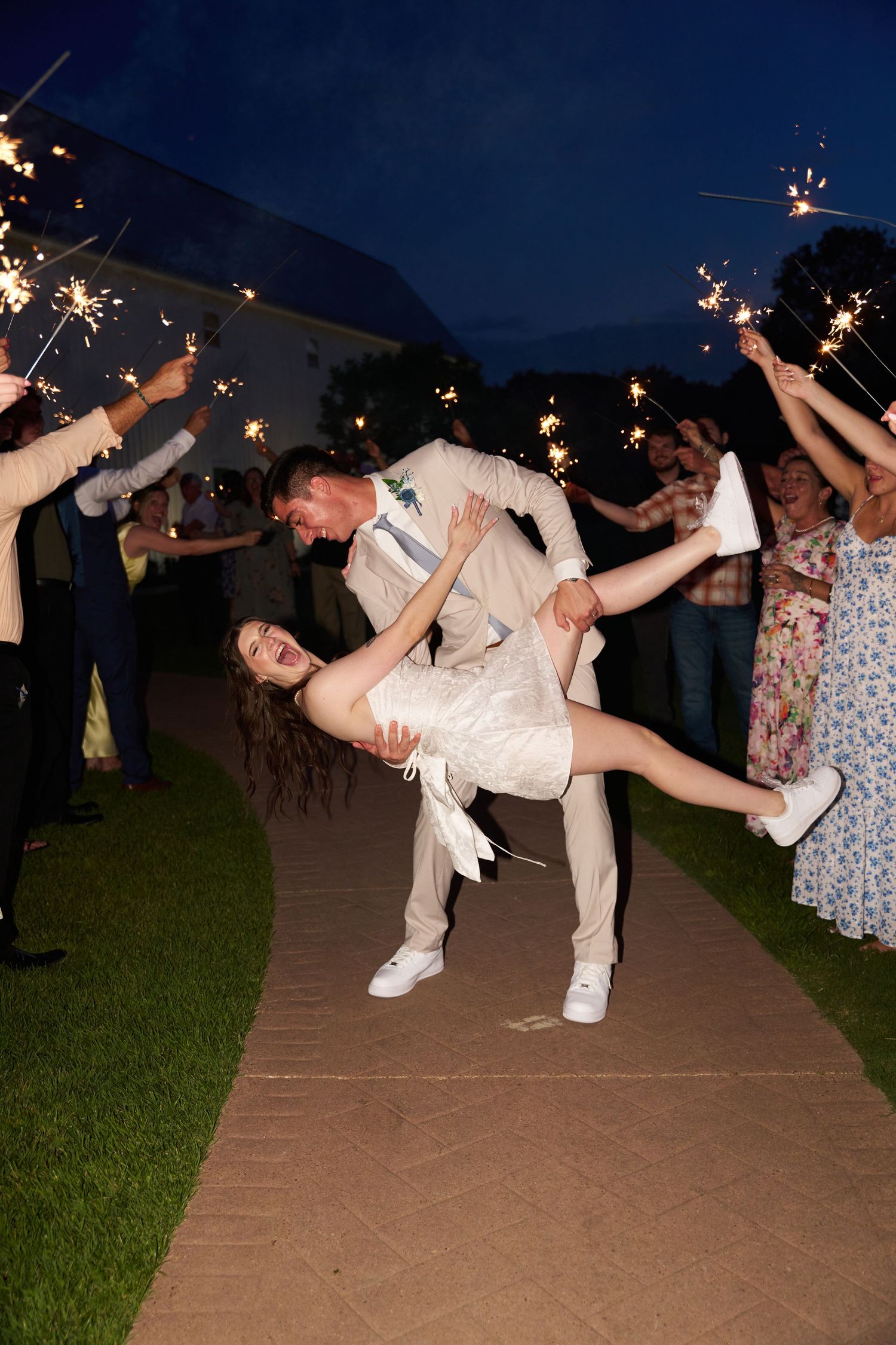 A romantic dip pose during a wedding celebration with sparklers glowing in the night sky at an outdoor venue.