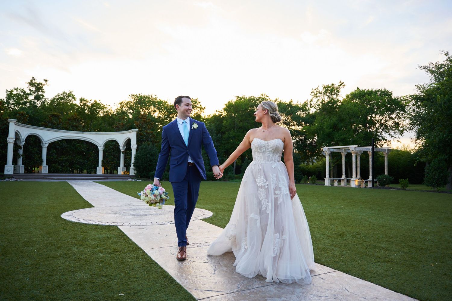 Wedding party walking on outdoor pathway with white gazebo in background.