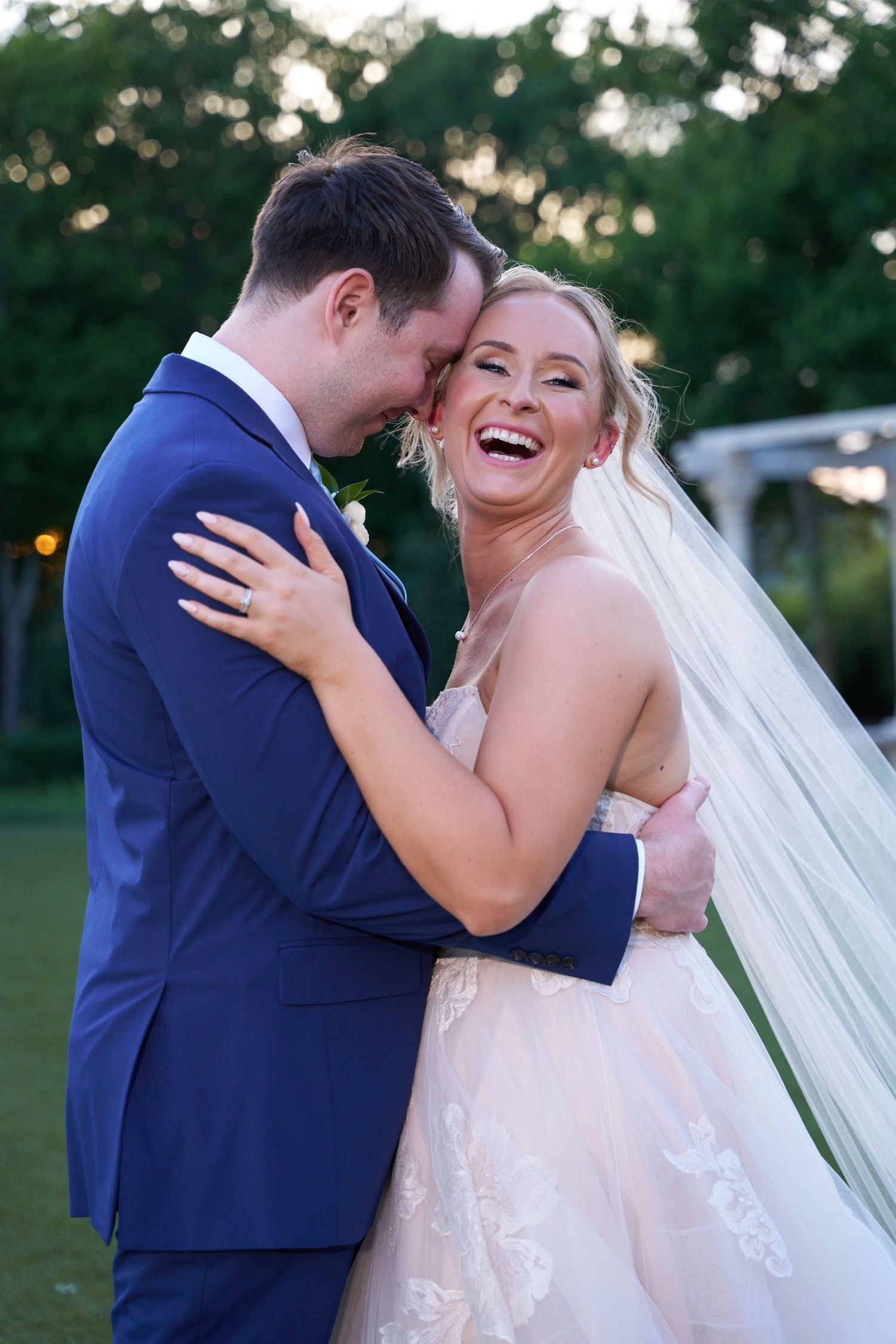 A romantic outdoor wedding moment showing joyful laughter during the couple's first look in a natural setting.