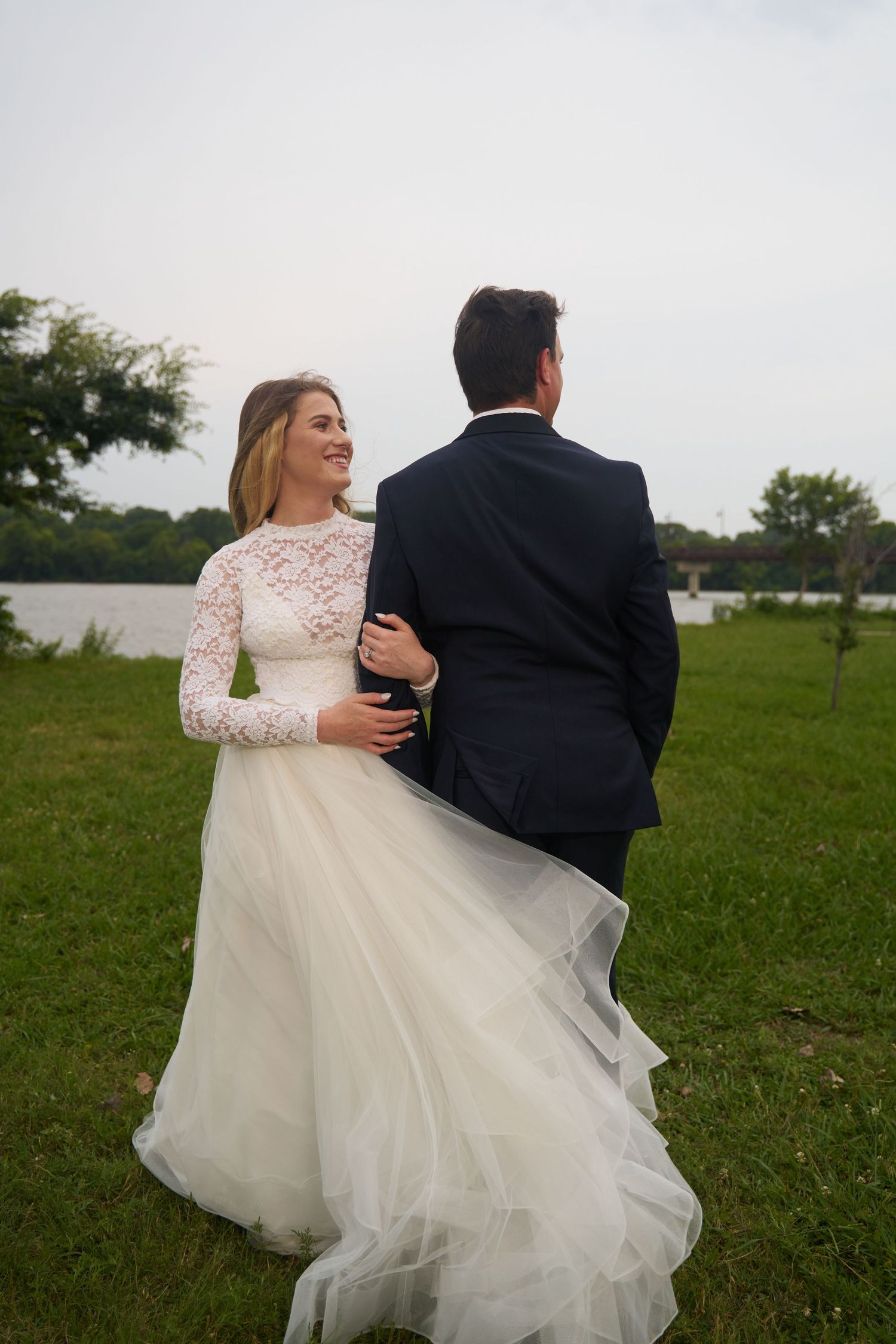 A couple in wedding attire embraces while spinning in a grassy field at sunset.