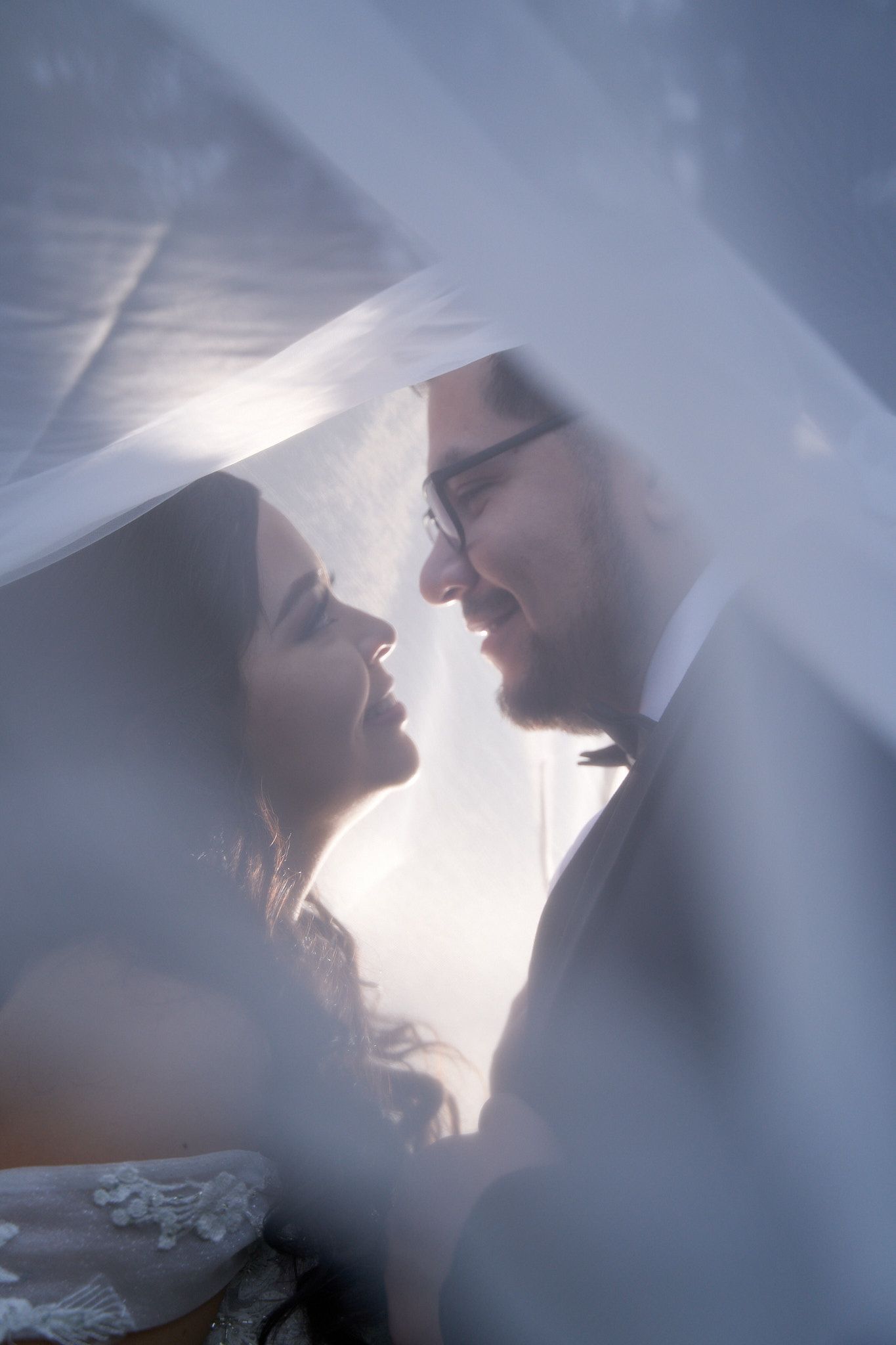 A dreamy, backlit silhouette of a couple through sheer fabric creates a romantic wedding portrait.
