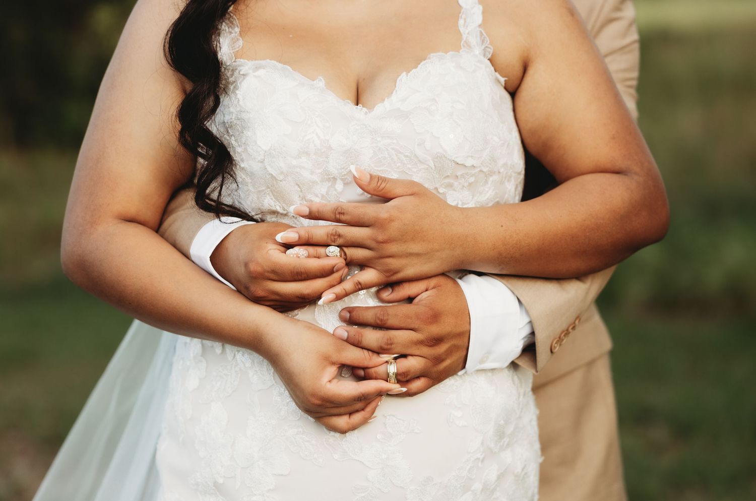 Close-up of hands with wedding rings against white lace dress details.