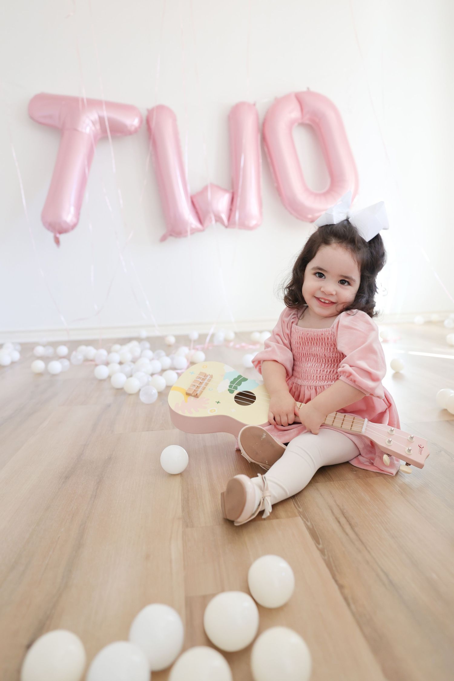 A toddler celebrating her 2nd birthday with a toy guitar during an indoor photoshoot in a playroom setting in Austin, TX.