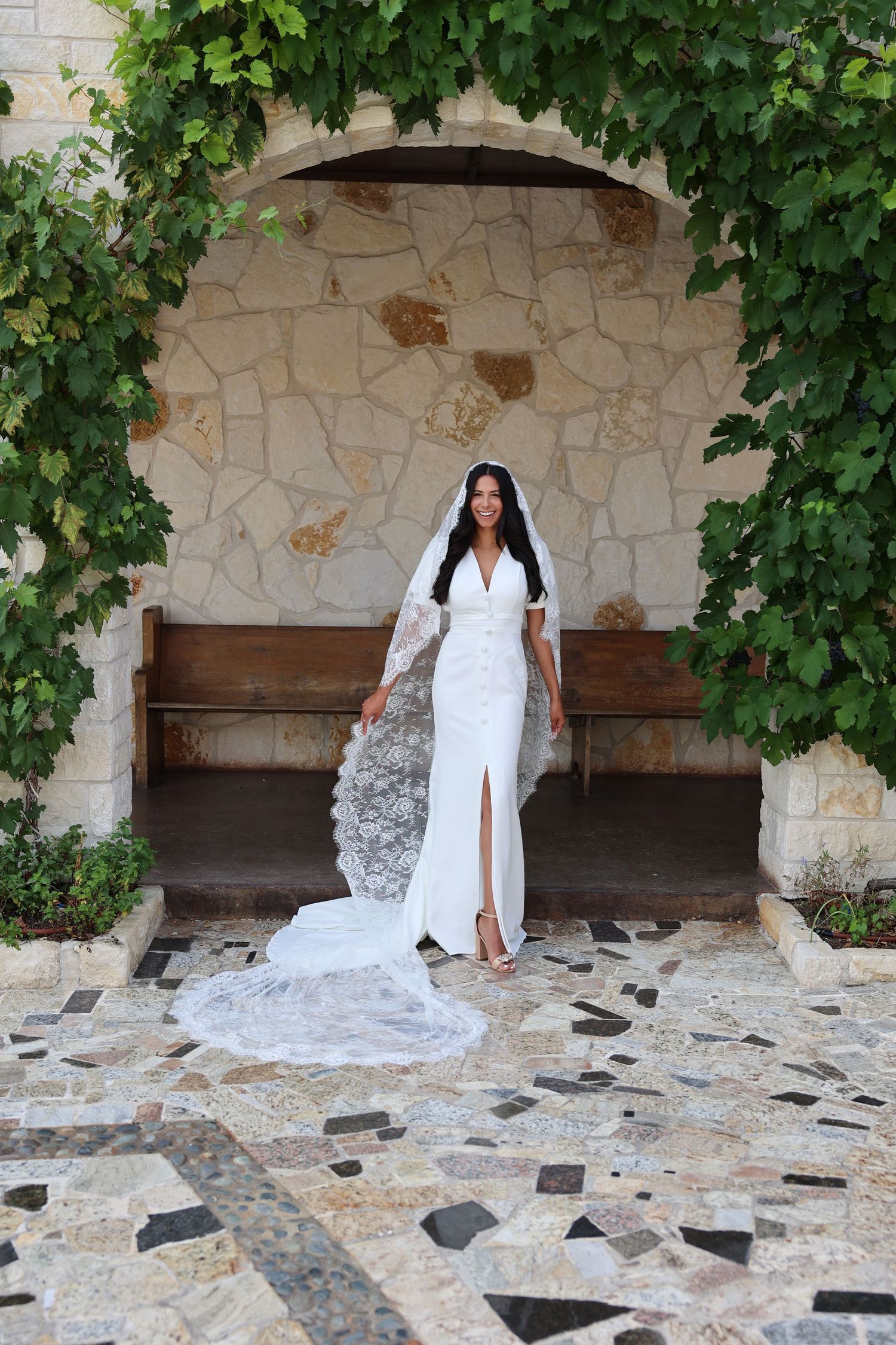 Wedding dress with flowing train photographed under stone archway with ivy.