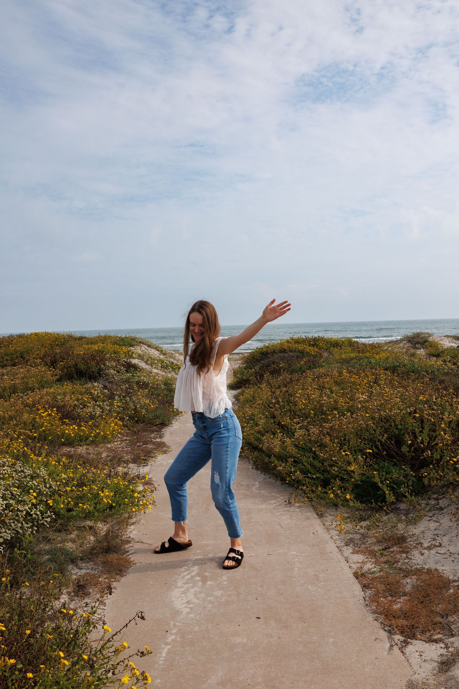 Carefree woman with arms spread wide on coastal path surrounded by yellow blooms.