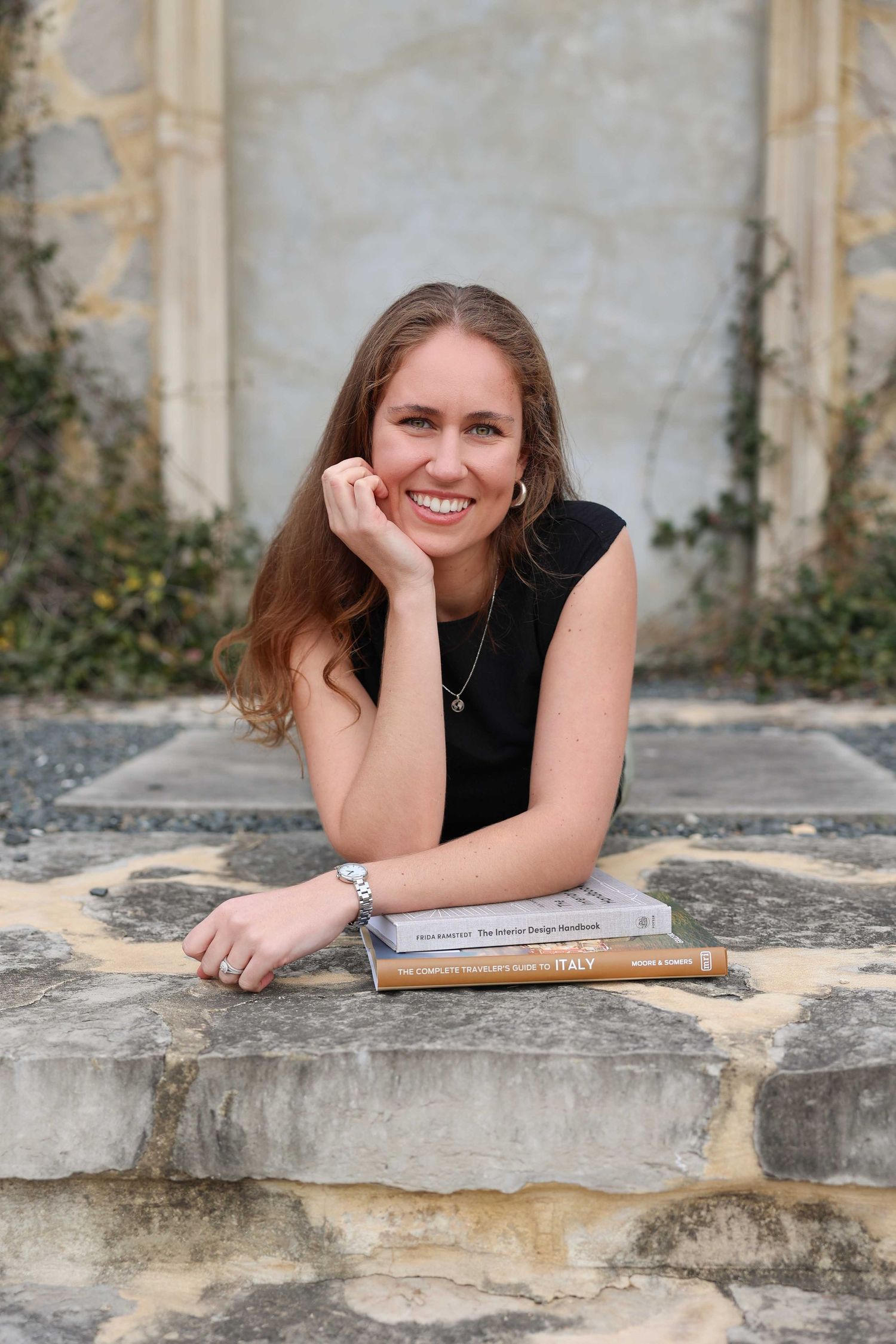 Person relaxing on stone steps with books while resting head on hand.