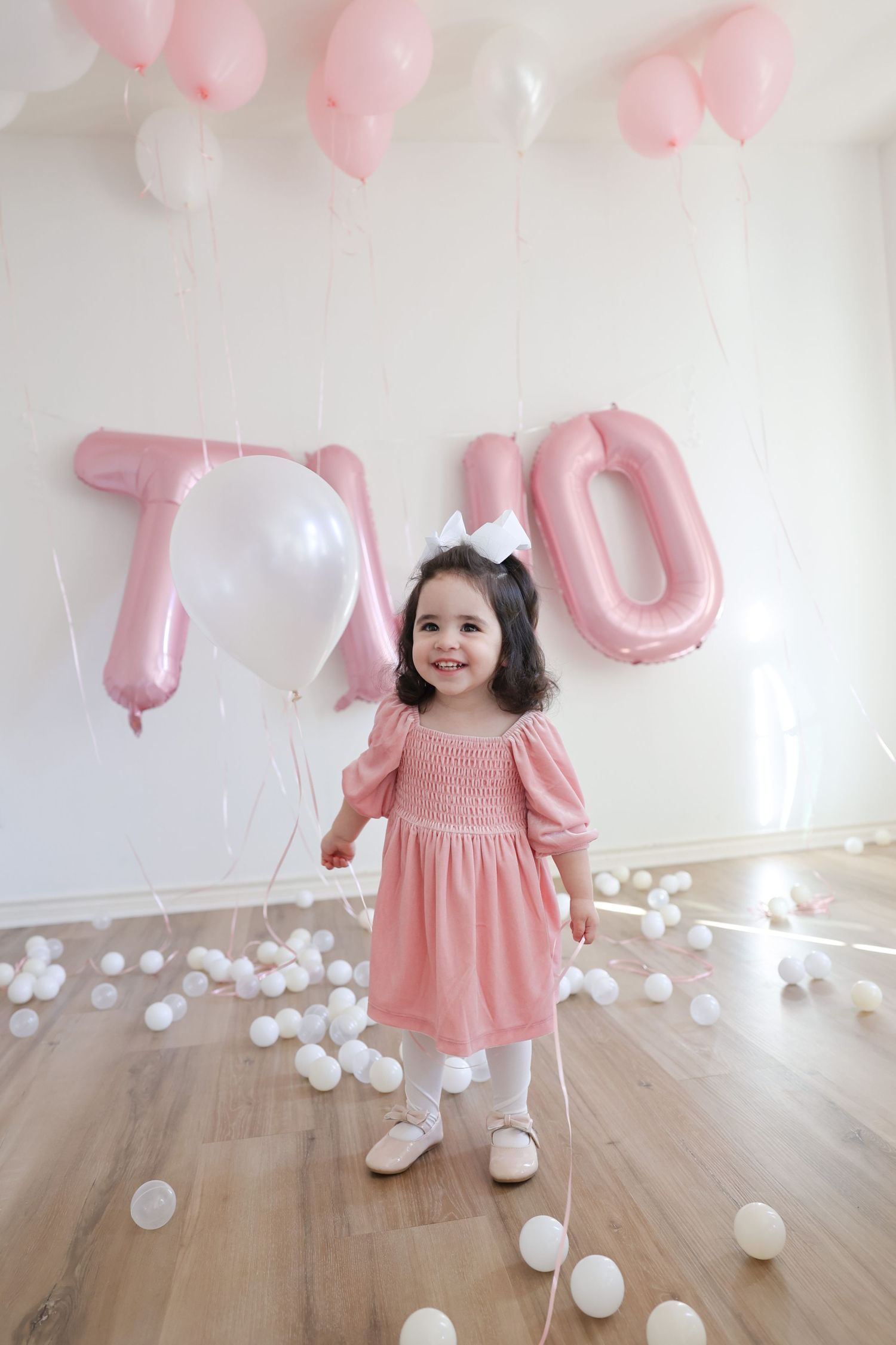A toddler celebrating their birthday during a studio photoshoot in Austin, TX with balloons and bows.