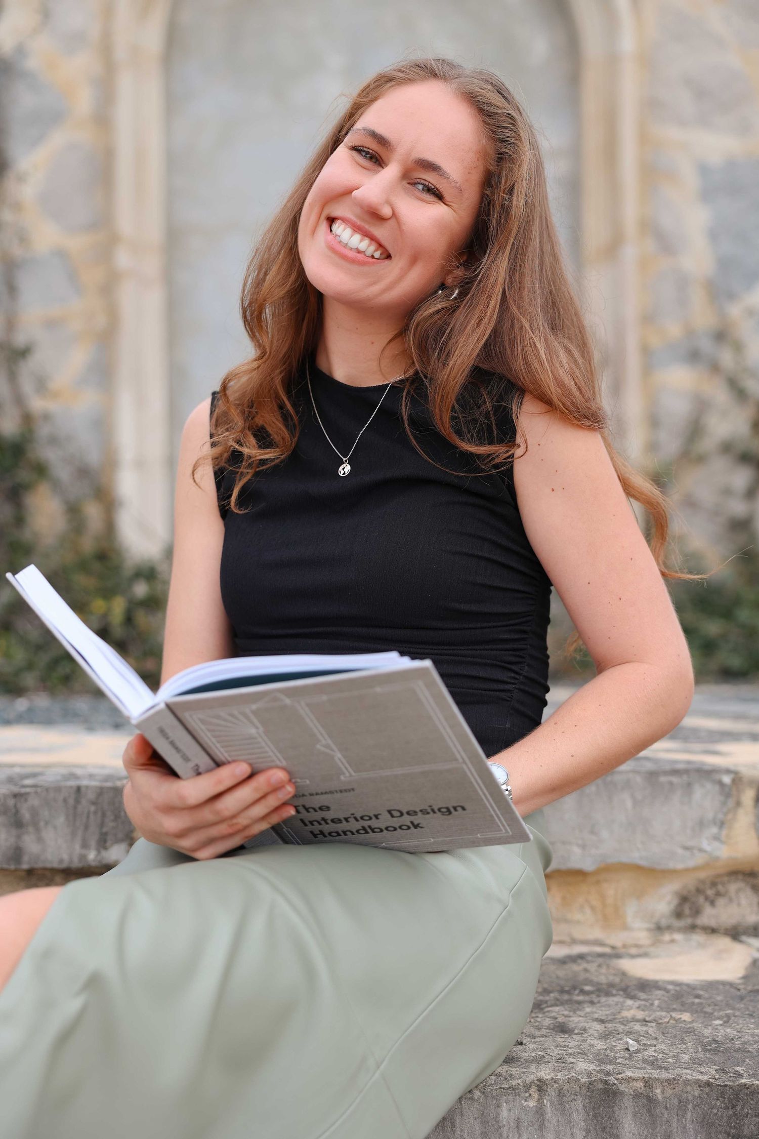 Person in black sleeveless top reading a book while sitting on stone steps with a joyful expression.