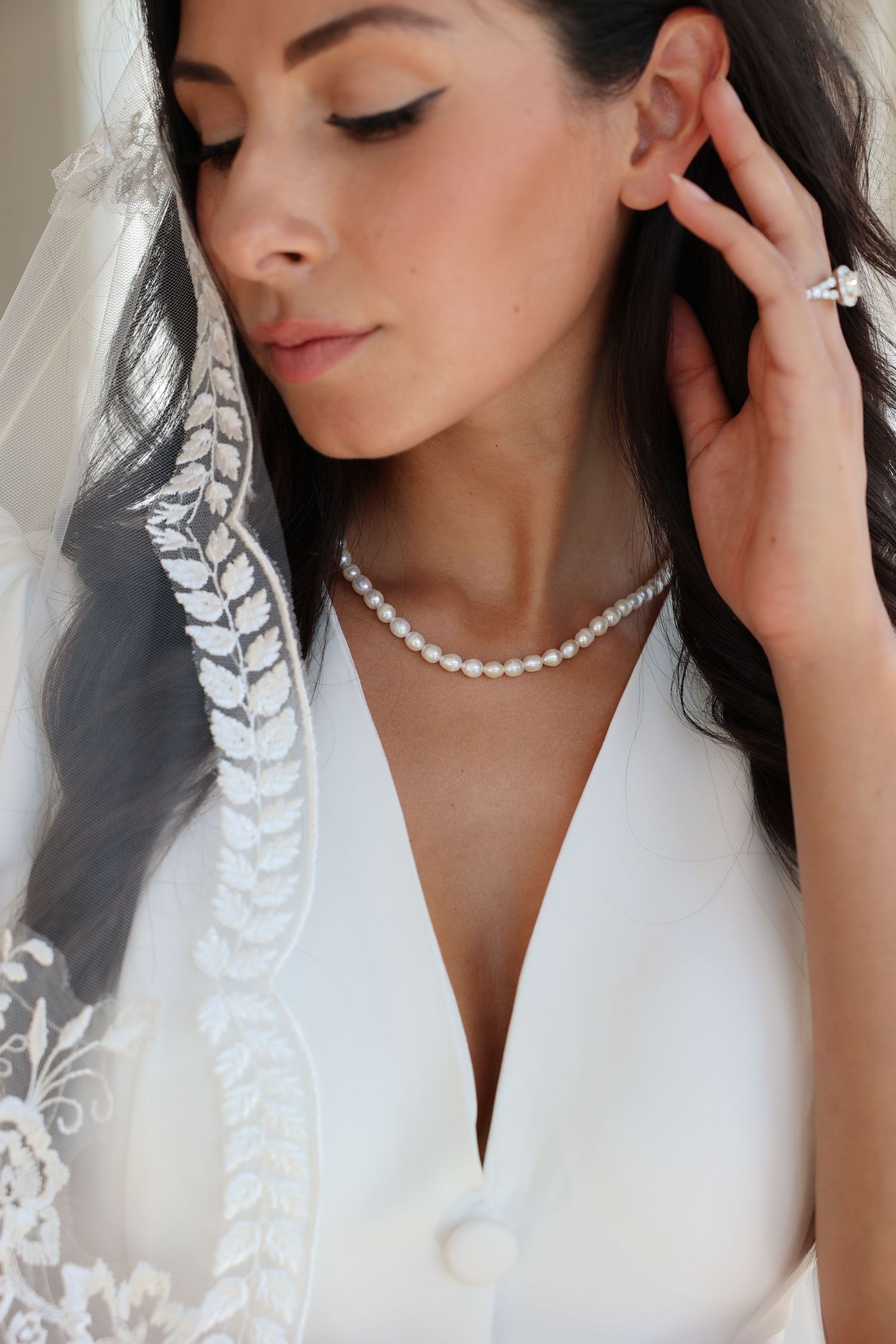 Close-up of bride wearing pearl necklace and lace veil with elegant makeup.