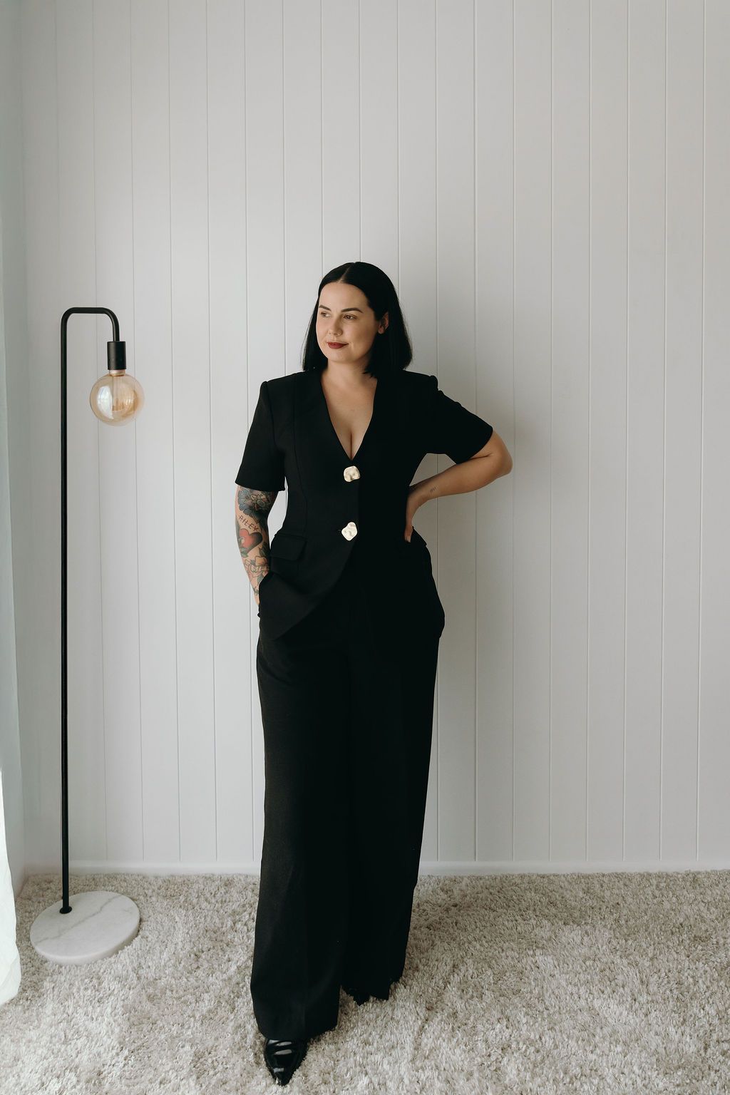 A series of fashion poses showing a person wearing a long black dress against a white wall with beige carpet.