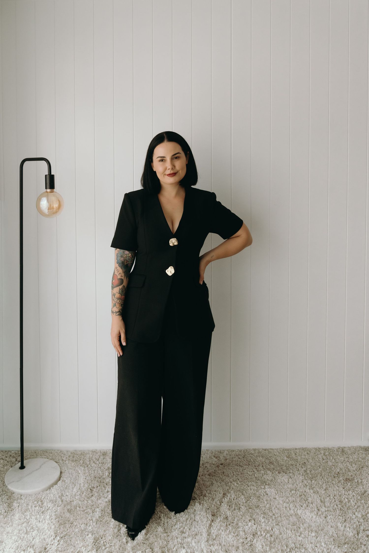 A person wearing a long black sleeveless dress poses against a white wall in a series of four fashion photos.