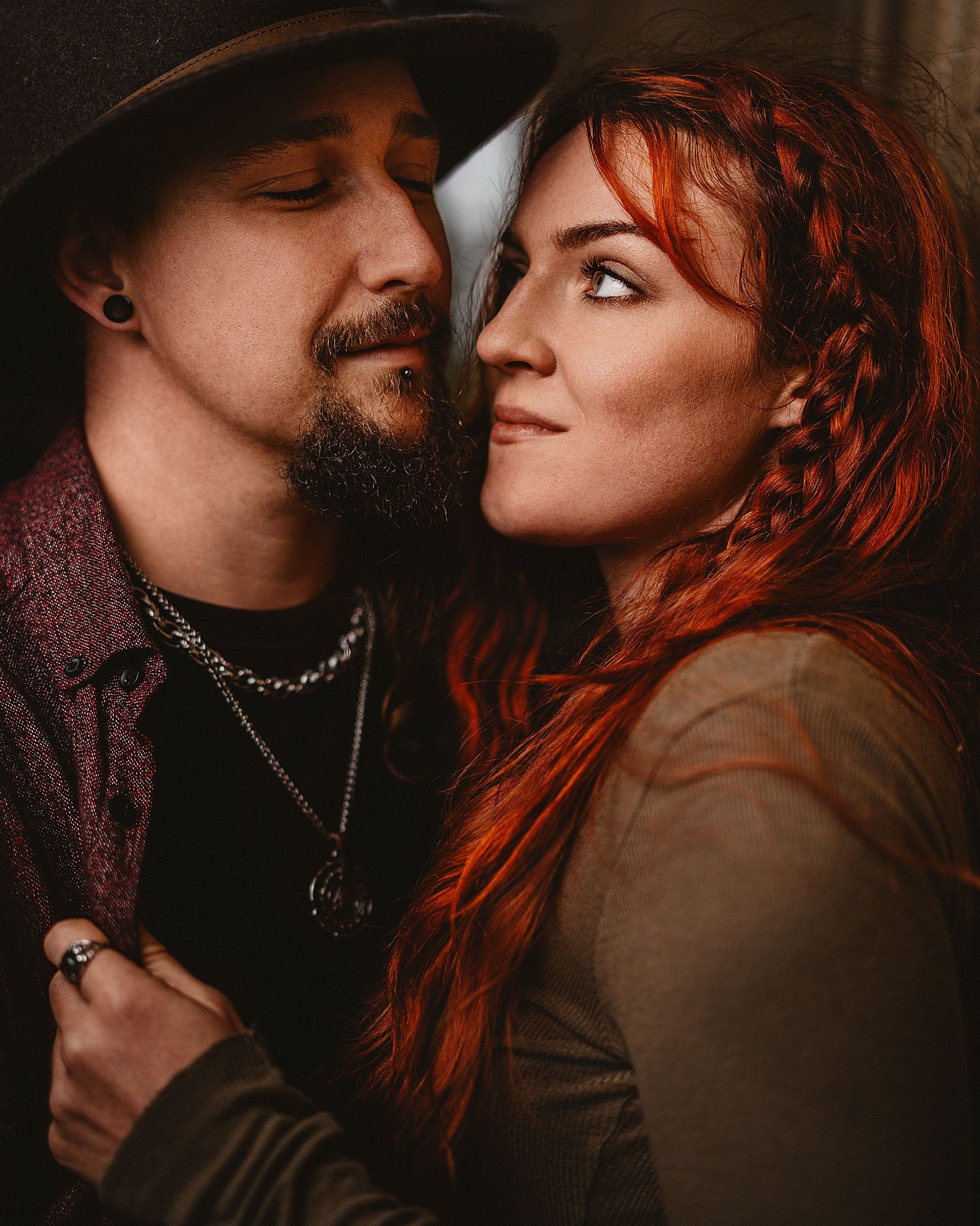 A romantic couple shares an intimate moment with dramatic lighting, featuring vibrant red hair and moody atmosphere.