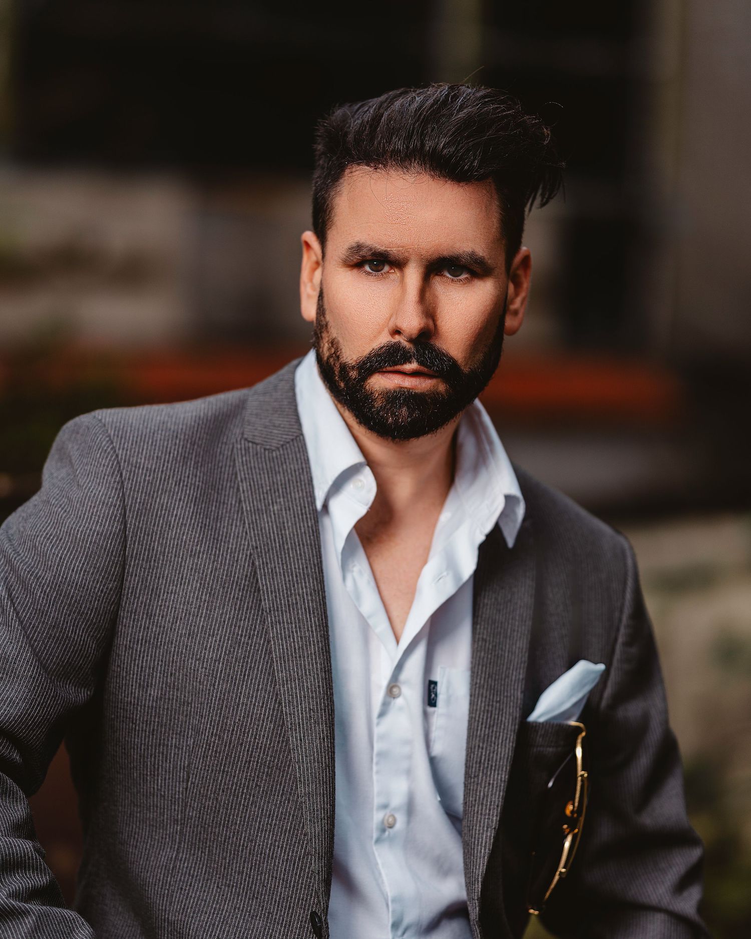 Professional portrait of someone wearing a gray suit jacket and white dress shirt in dramatic lighting.