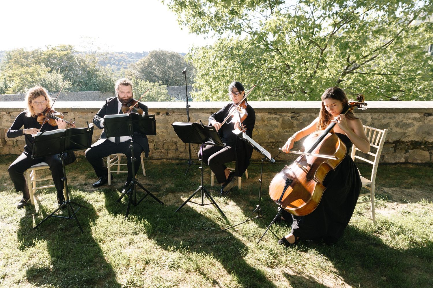 String quartet performing outdoors on sunny day at elegant wedding ceremony venue.