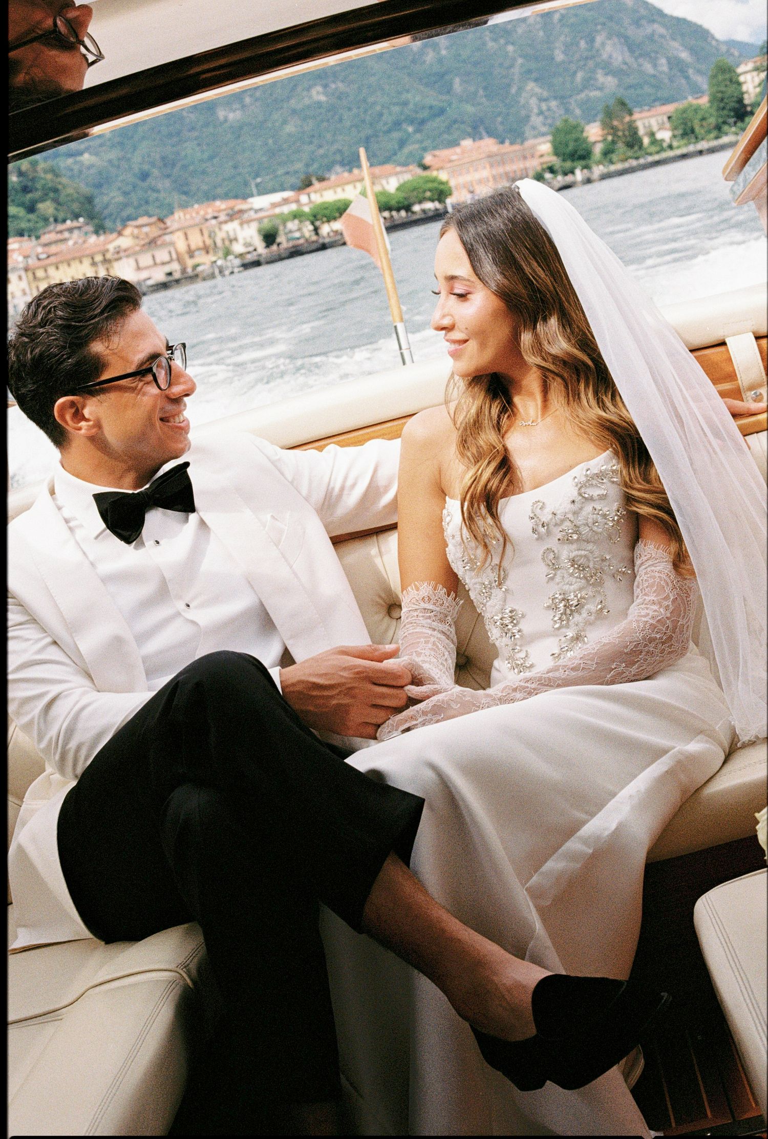 Bride and groom share a romantic moment on a luxury boat with Lake Como's scenic shoreline in the background.