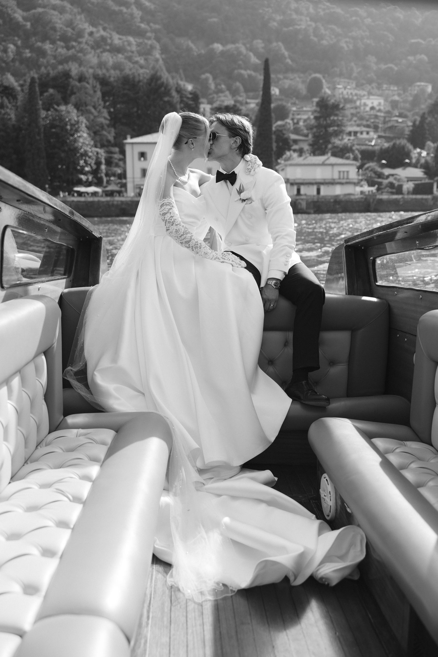 Black and white photo of bride and groom kissing on a luxury boat with scenic hills in the background.
