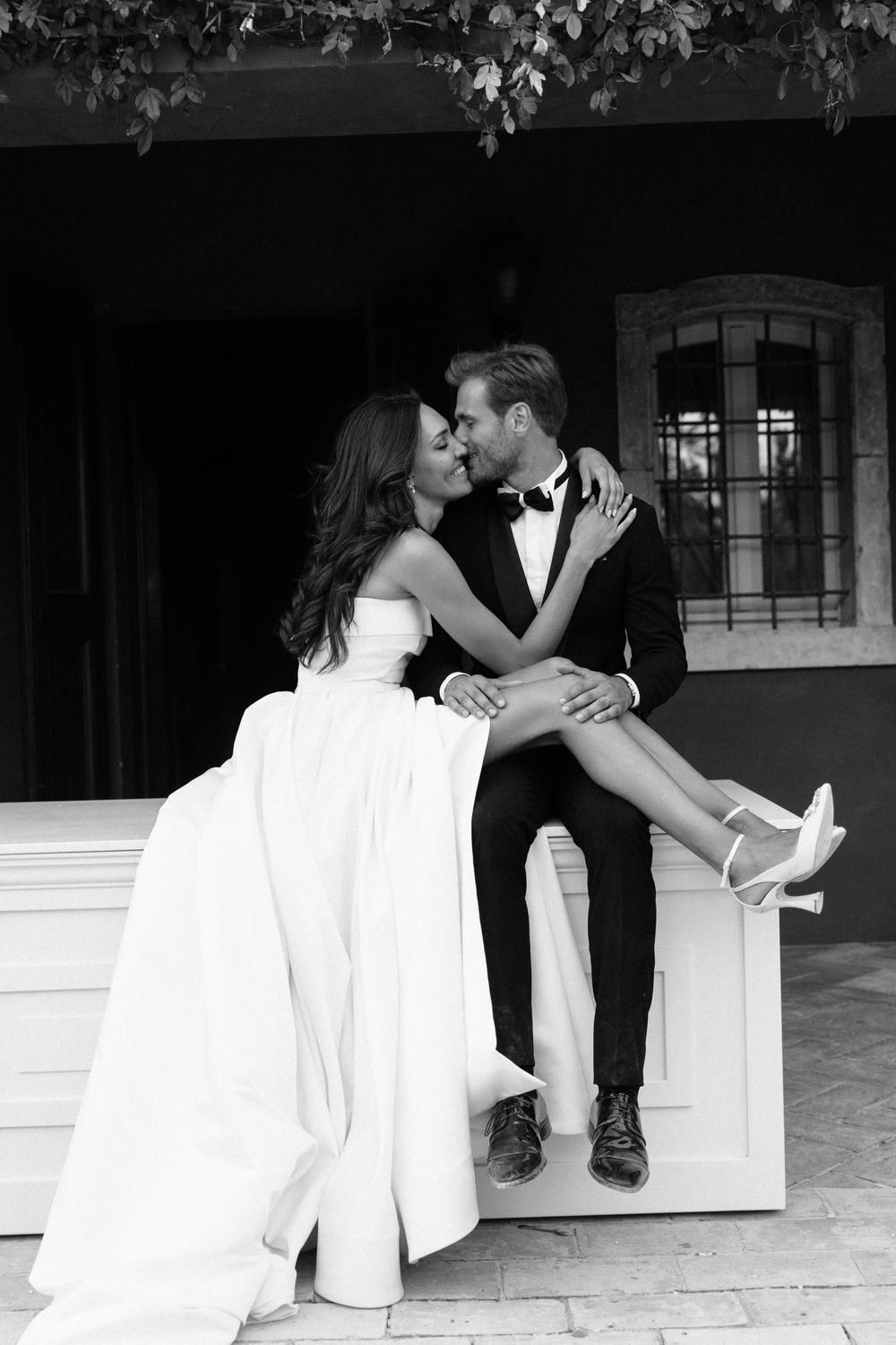 Black and white photo of bride and groom sharing a kiss while seated on steps.