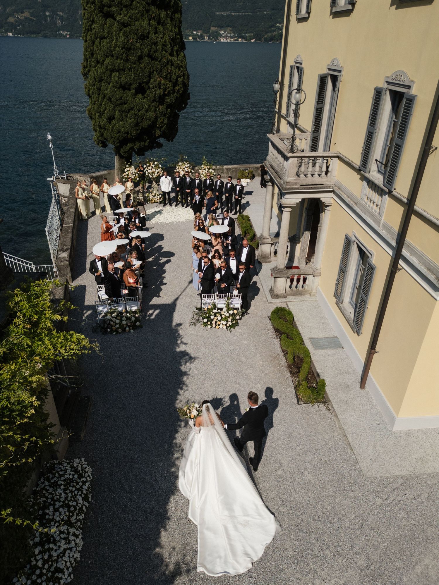 Aerial view of an outdoor wedding ceremony at an elegant Italian villa on Lake Como, with bride and groom approaching guests.