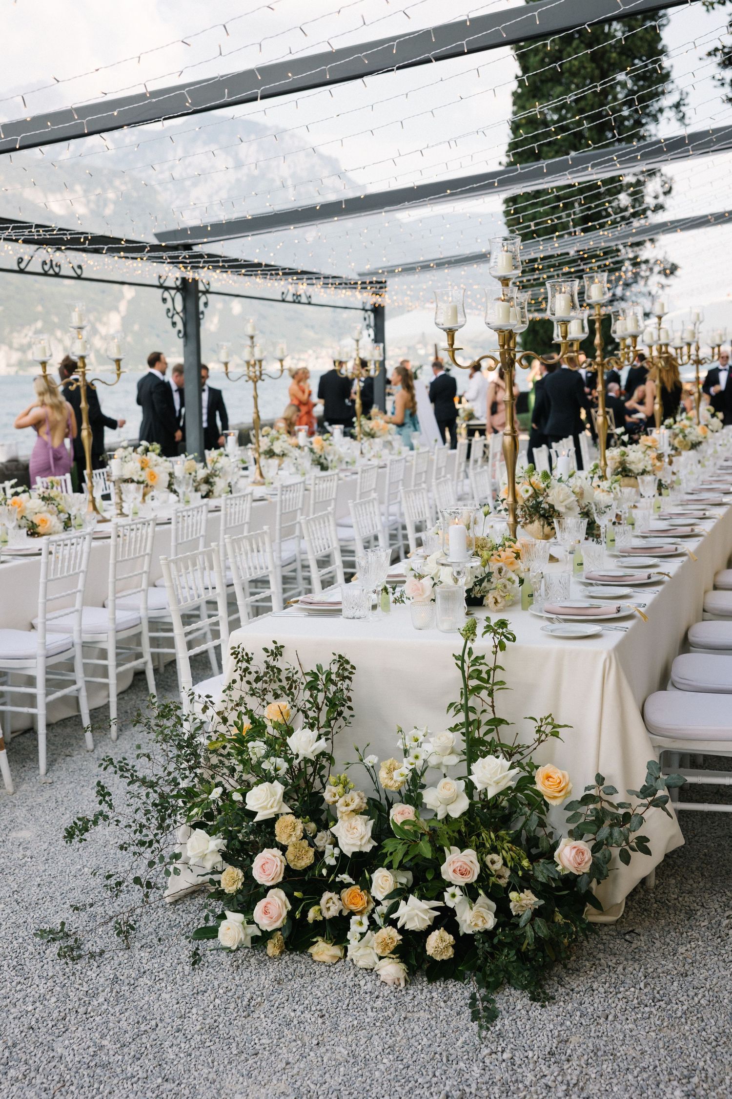 Elegant outdoor wedding reception with white floral arrangements, Chiavari chairs, and candelabras under a clear tent.