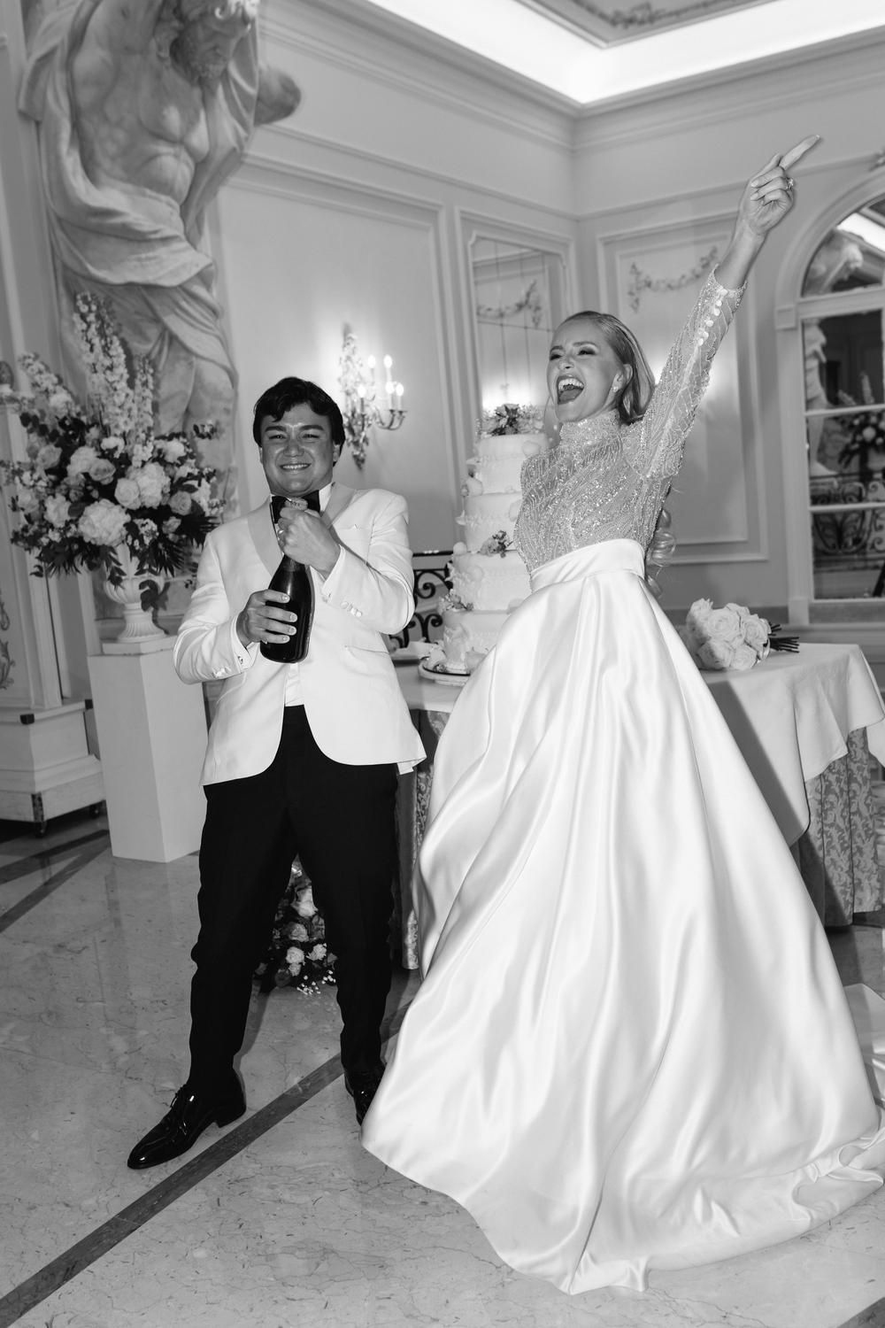 Black and white photo of bride and groom celebrating with champagne at elegant wedding reception.
