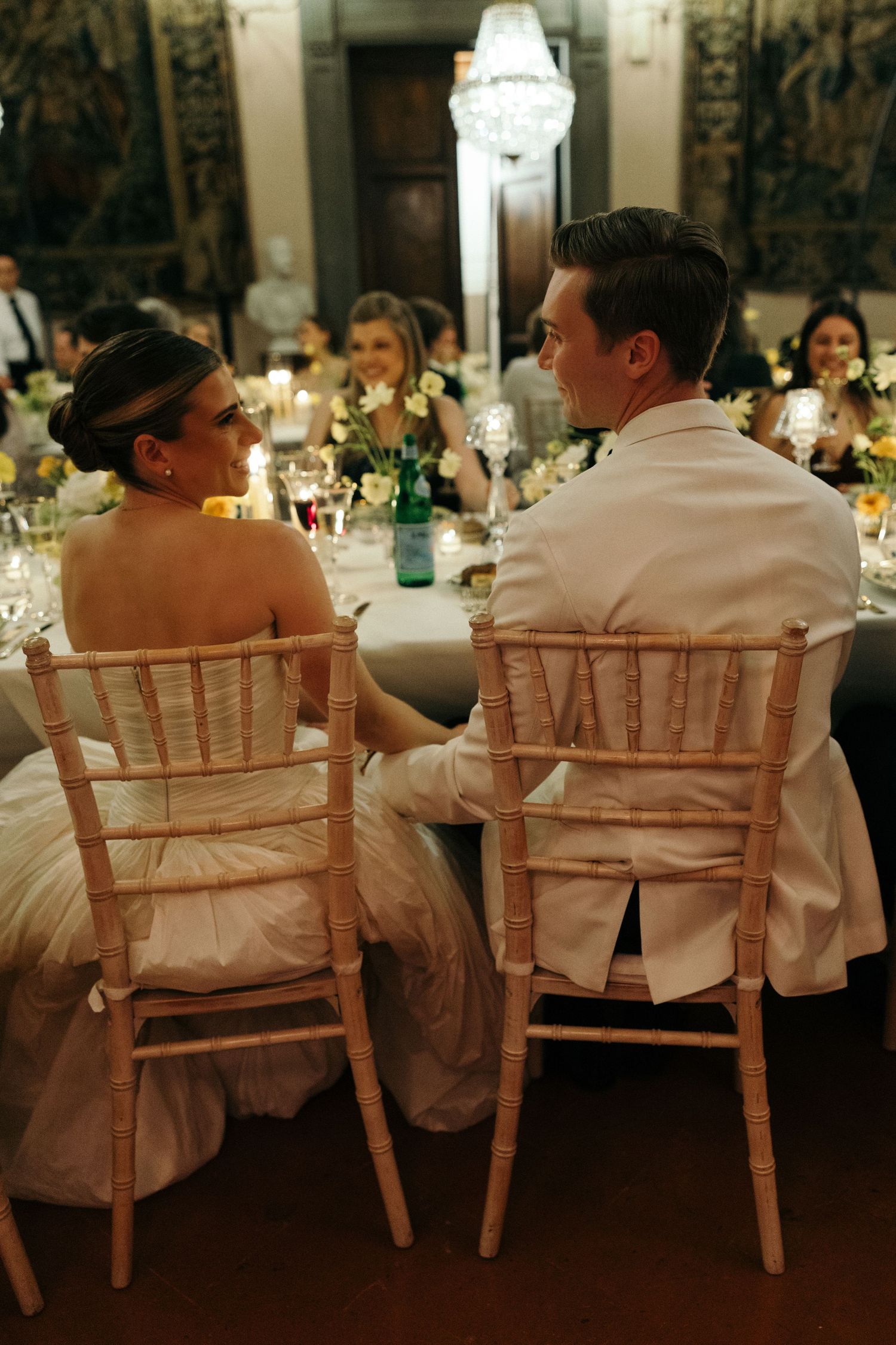 Bride and groom sit together at their wedding reception dinner table in an elegant candlelit venue.