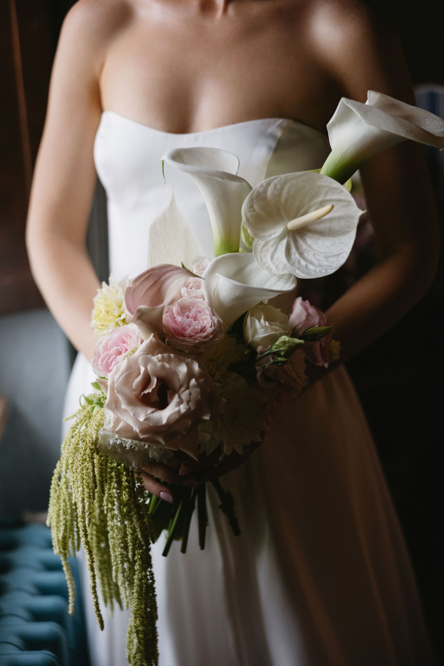 Bride holding elegant wedding bouquet with white calla lilies, pink roses, anthurium, and cascading green amaranthus.