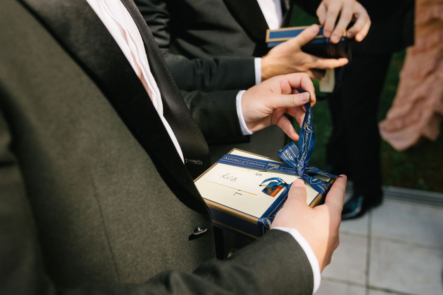 Man in suit opening a navy blue gift box tied with a ribbon at a formal event.