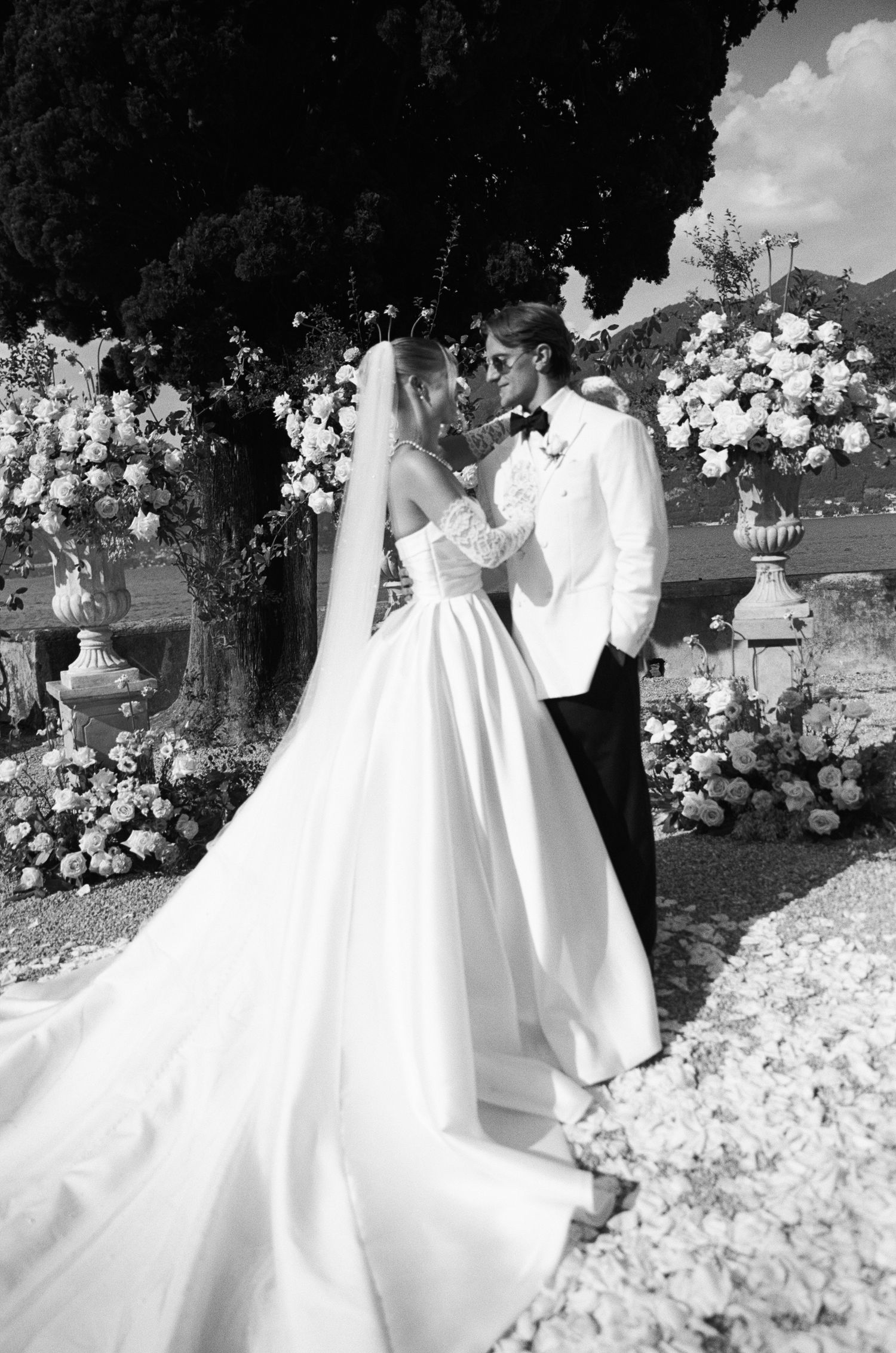 Bride and groom share first kiss surrounded by lush floral arrangements at outdoor wedding ceremony.