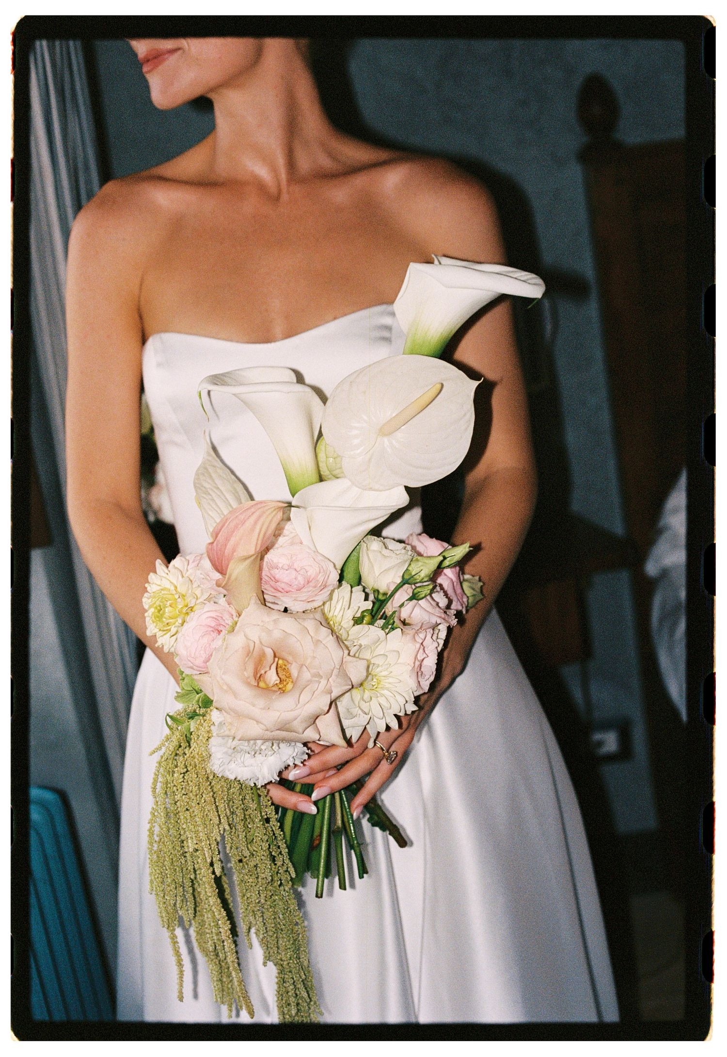 Bride in strapless white gown holding elegant bouquet of calla lilies, pink ranunculus, and green amaranthus.