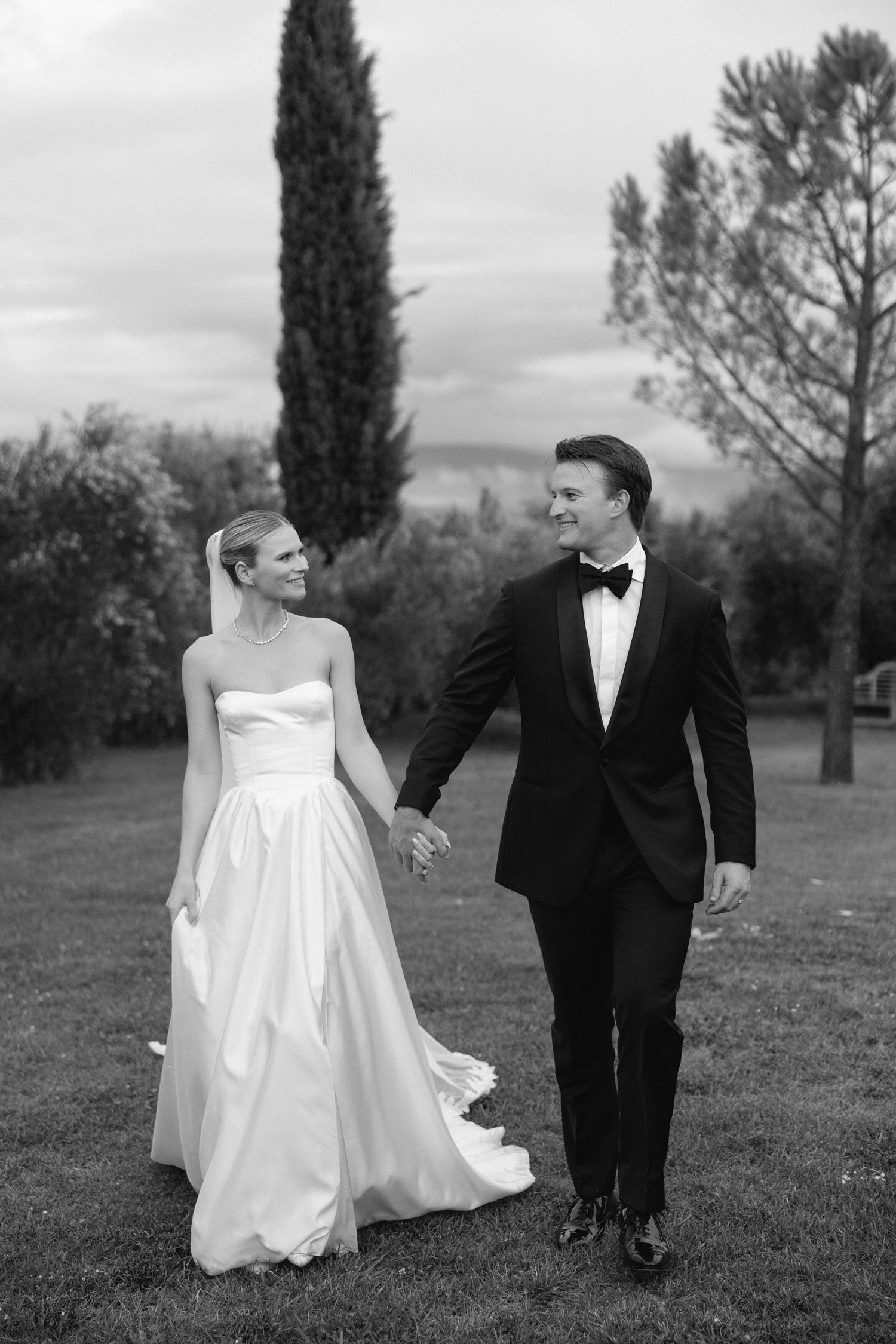 Black and white photo of a bride and groom holding hands walking outdoors on their wedding day.
