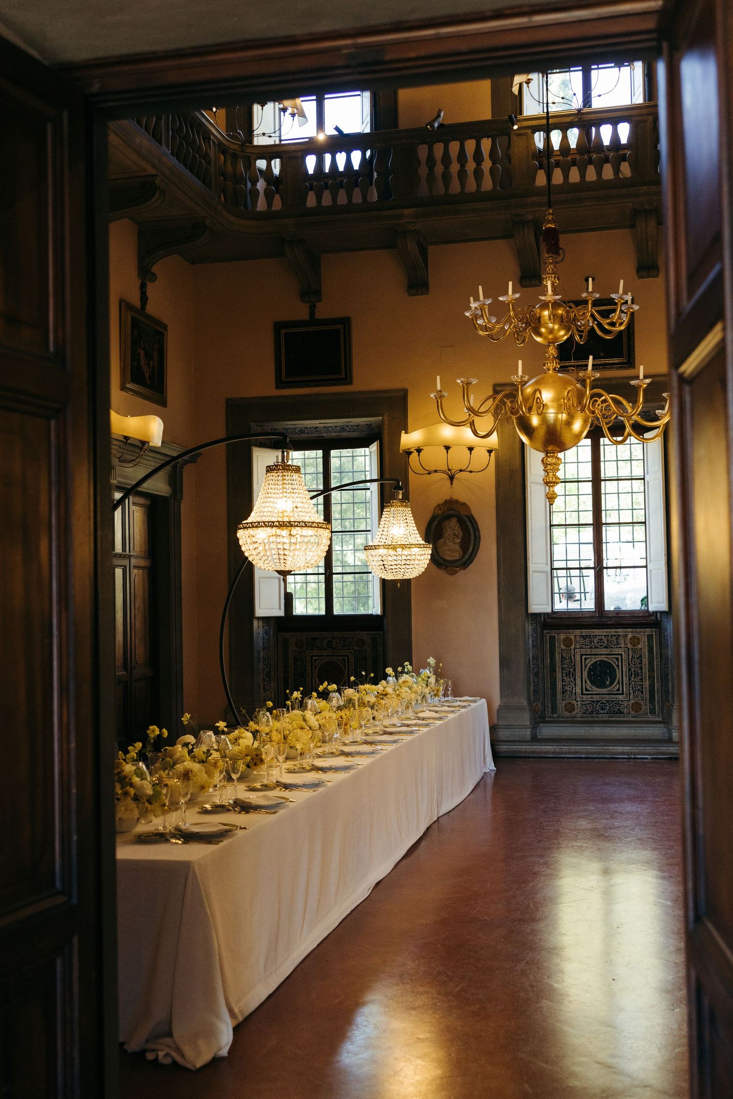 Elegant wedding reception table set beneath crystal chandeliers in a grand historic villa dining room.