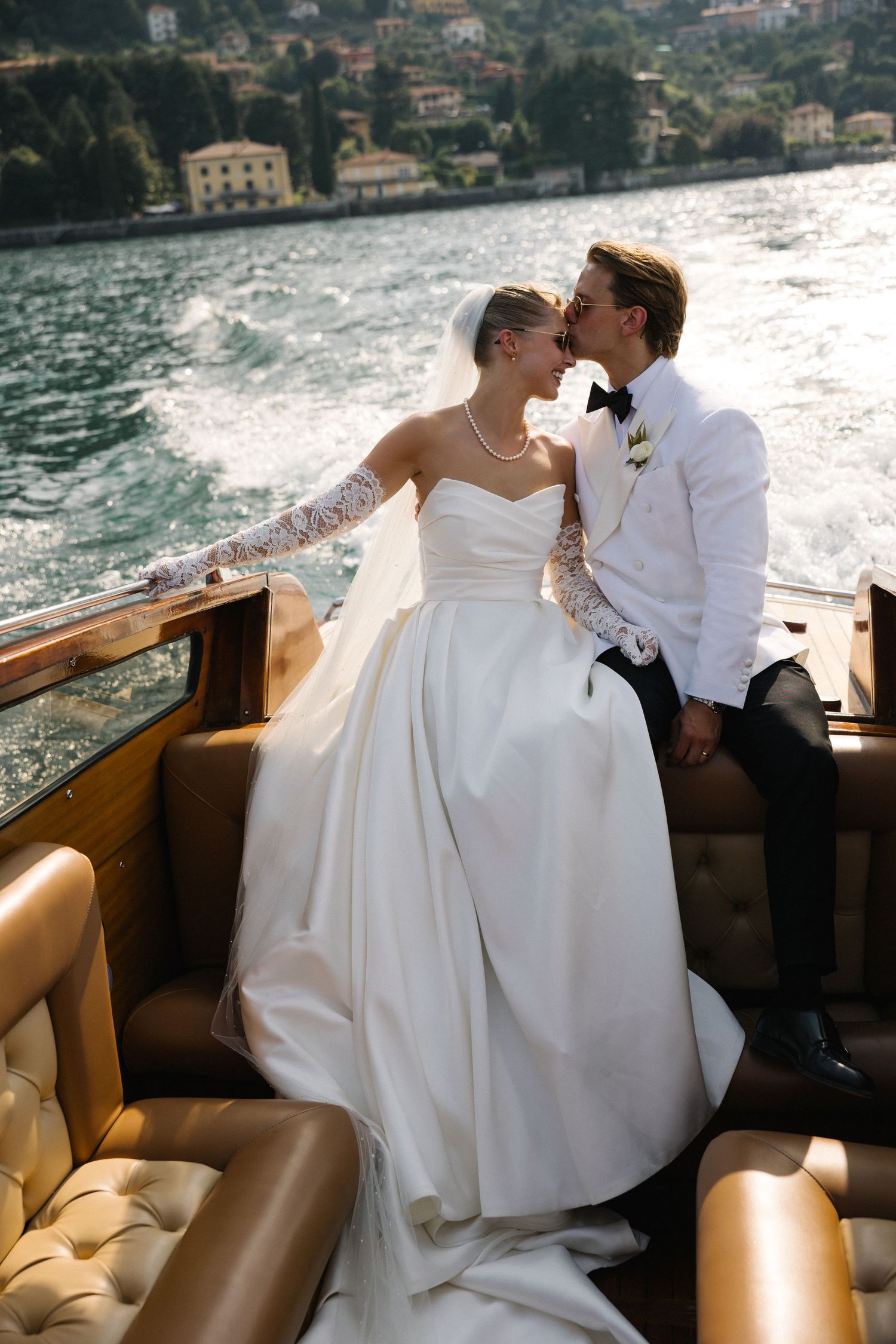 Bride and groom share a romantic kiss on a luxury boat on Lake Como, bride in elegant white gown with lace sleeves.