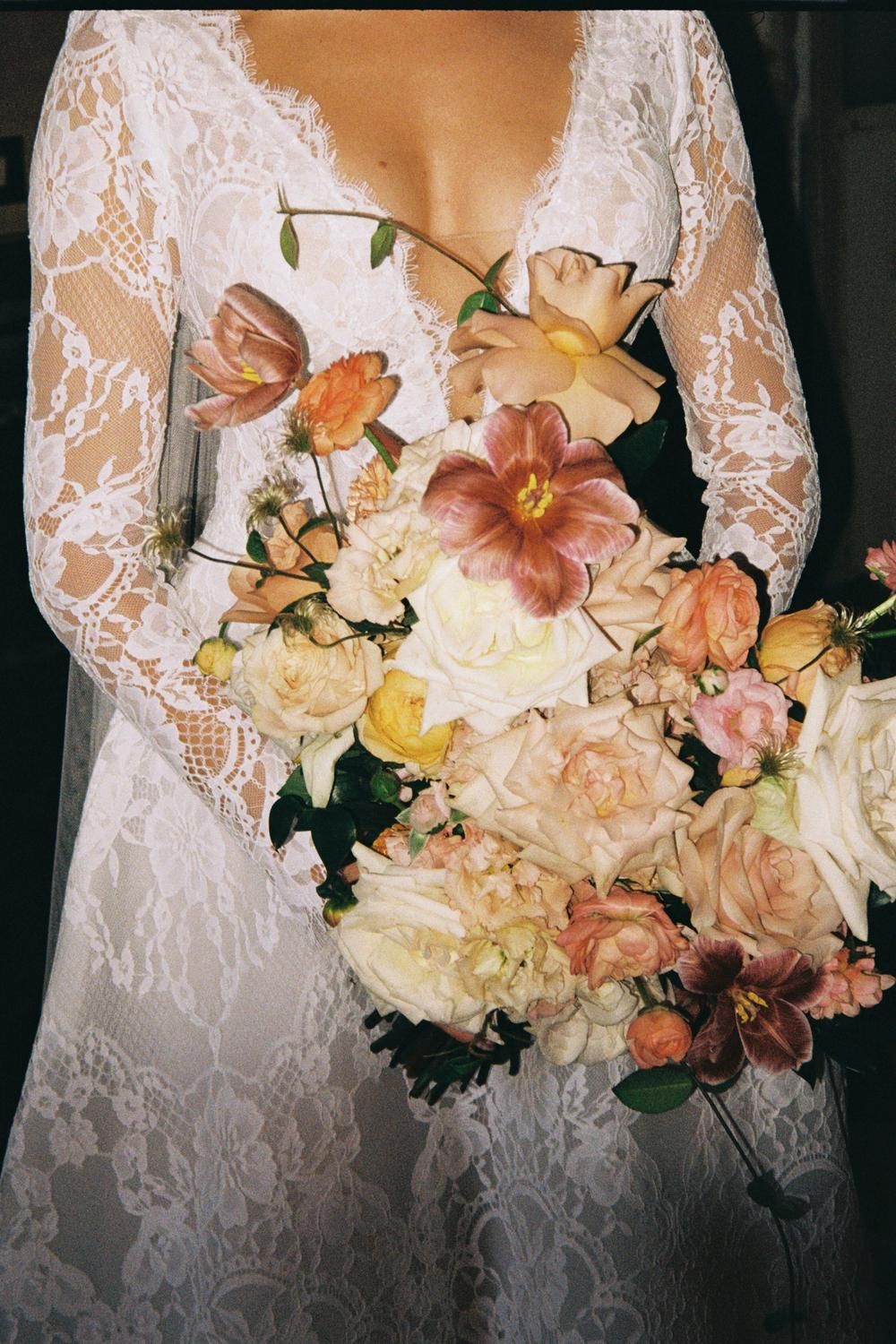 Bride in lace long-sleeve wedding dress holding lush peach and cream floral bouquet.