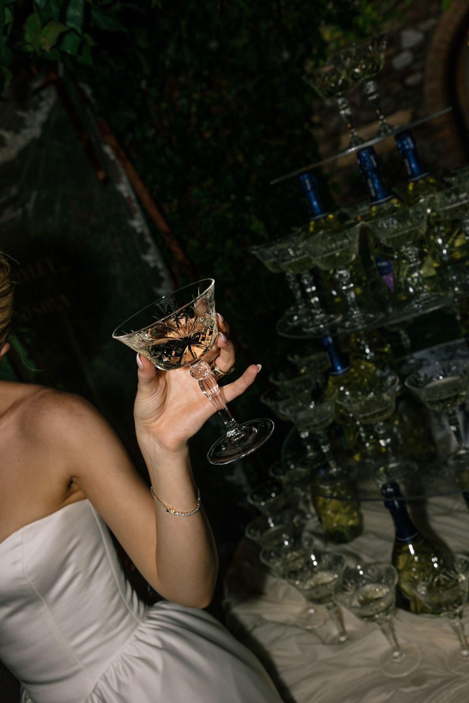 Bride in white strapless gown holding decorative champagne glass near elegant crystal tower at wedding reception.