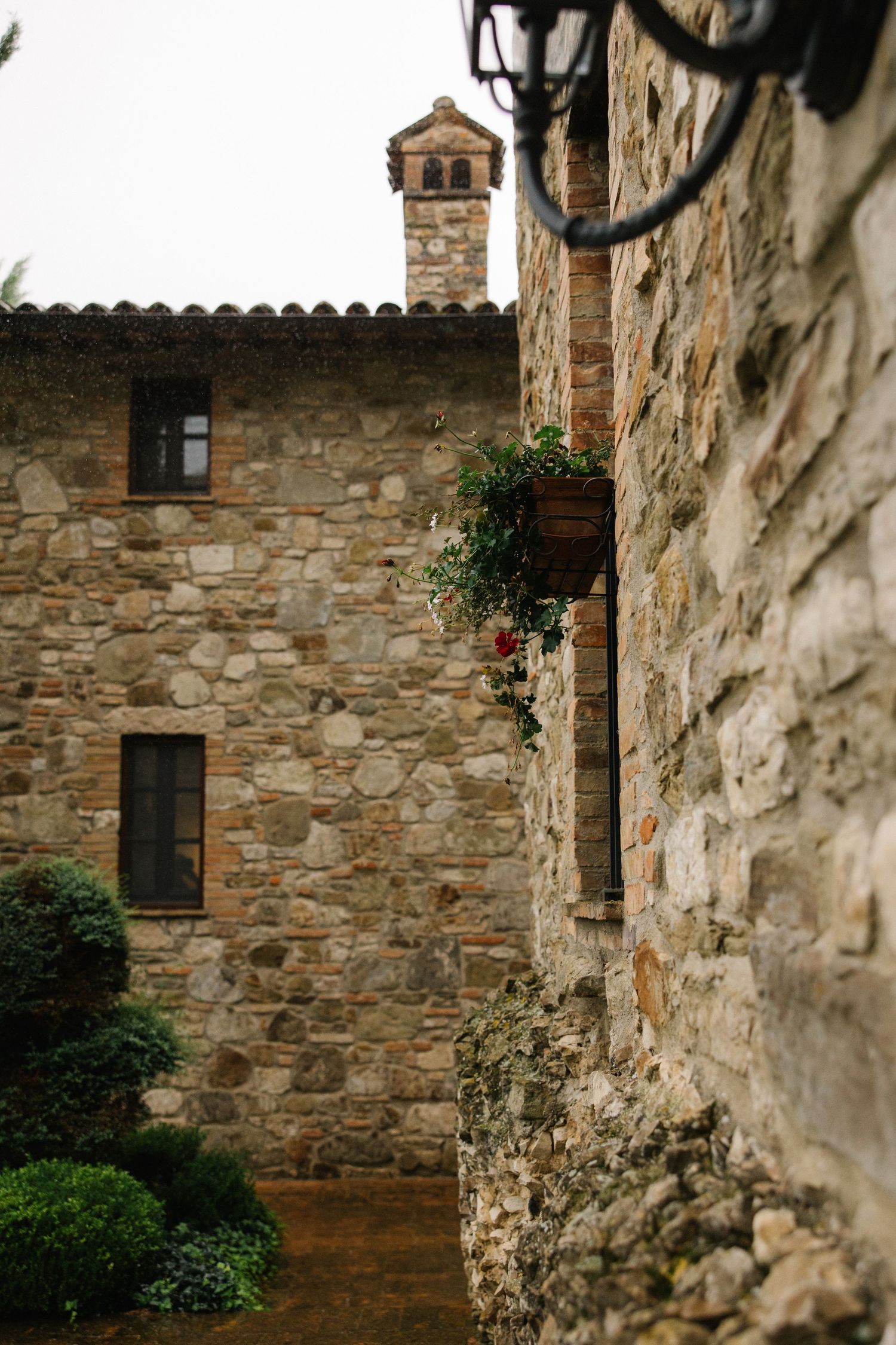 Historic Italian stone villa exterior with terracotta roof tiles, chimney, and climbing floral wall decor.
