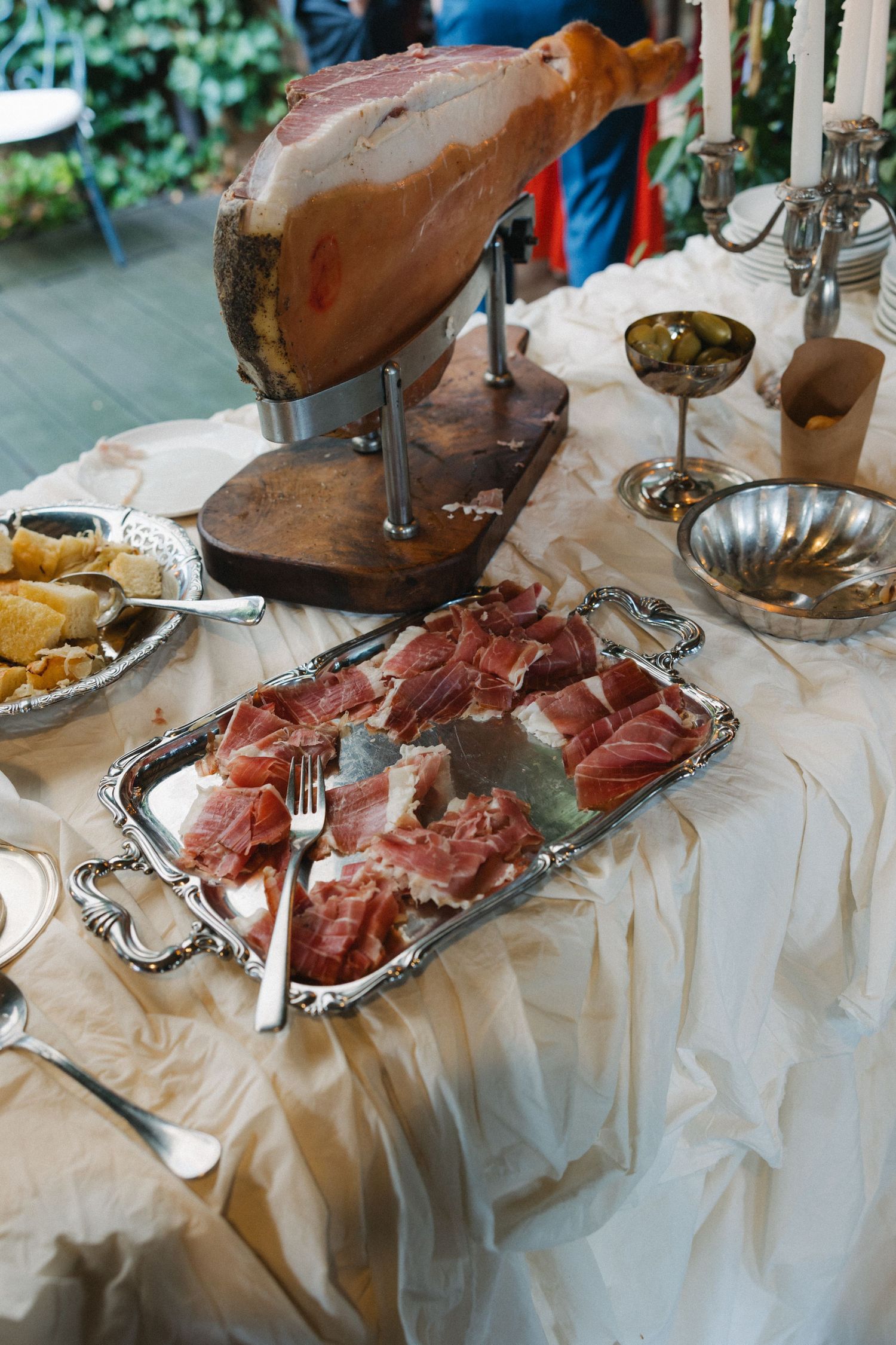 Elegant charcuterie display with sliced prosciutto on silver tray beside whole cured ham leg on wooden stand.