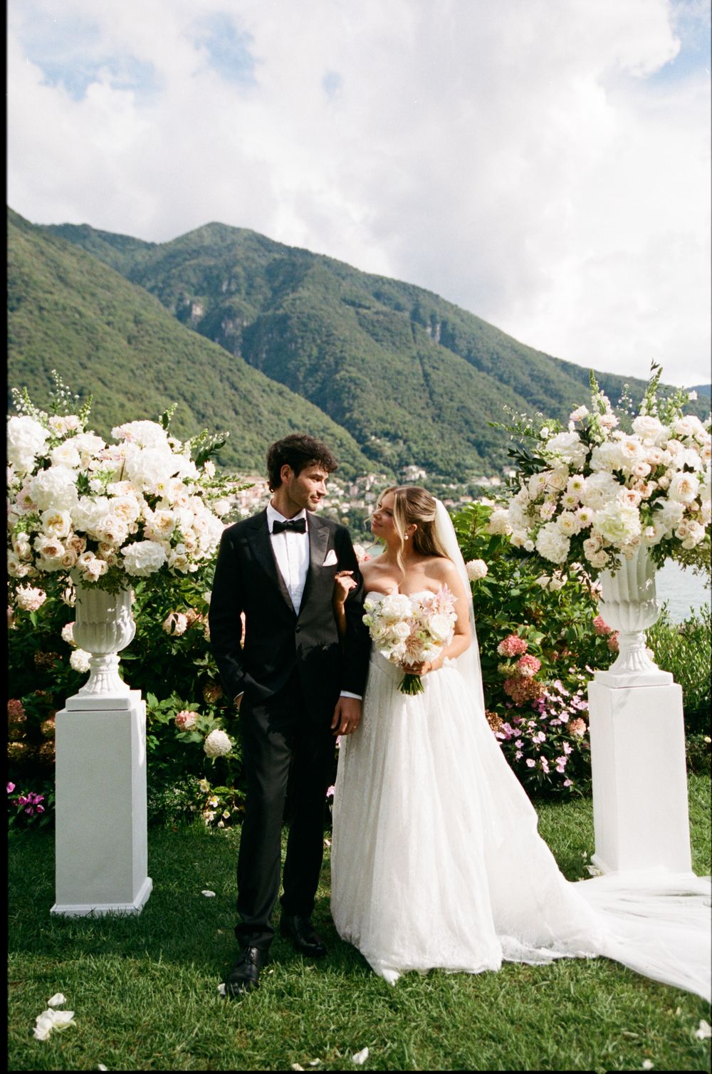 Bride and groom at altar with white floral arrangements and stunning mountain lake backdrop.
