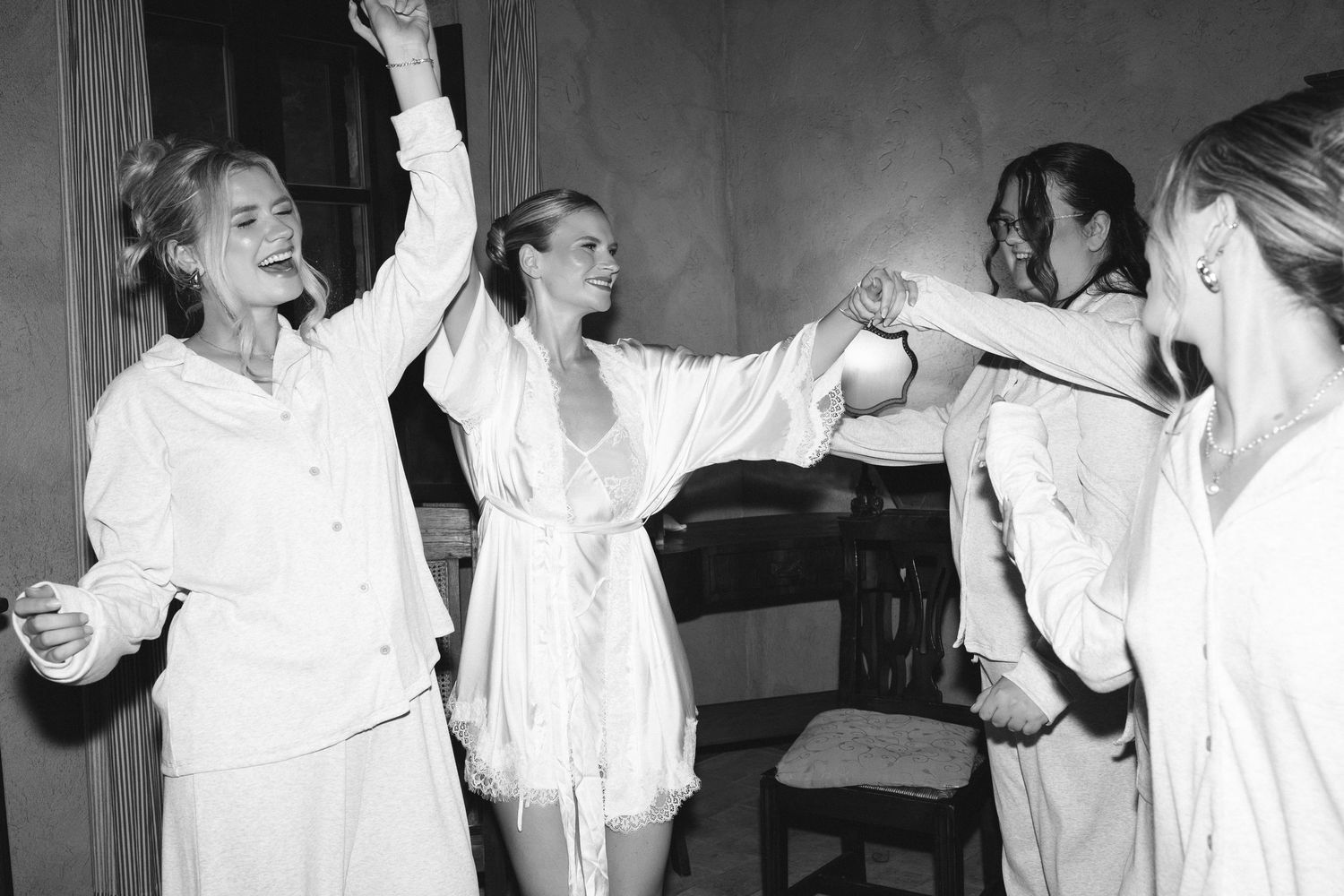 Women in white outfits dancing joyfully together in a black and white photo.