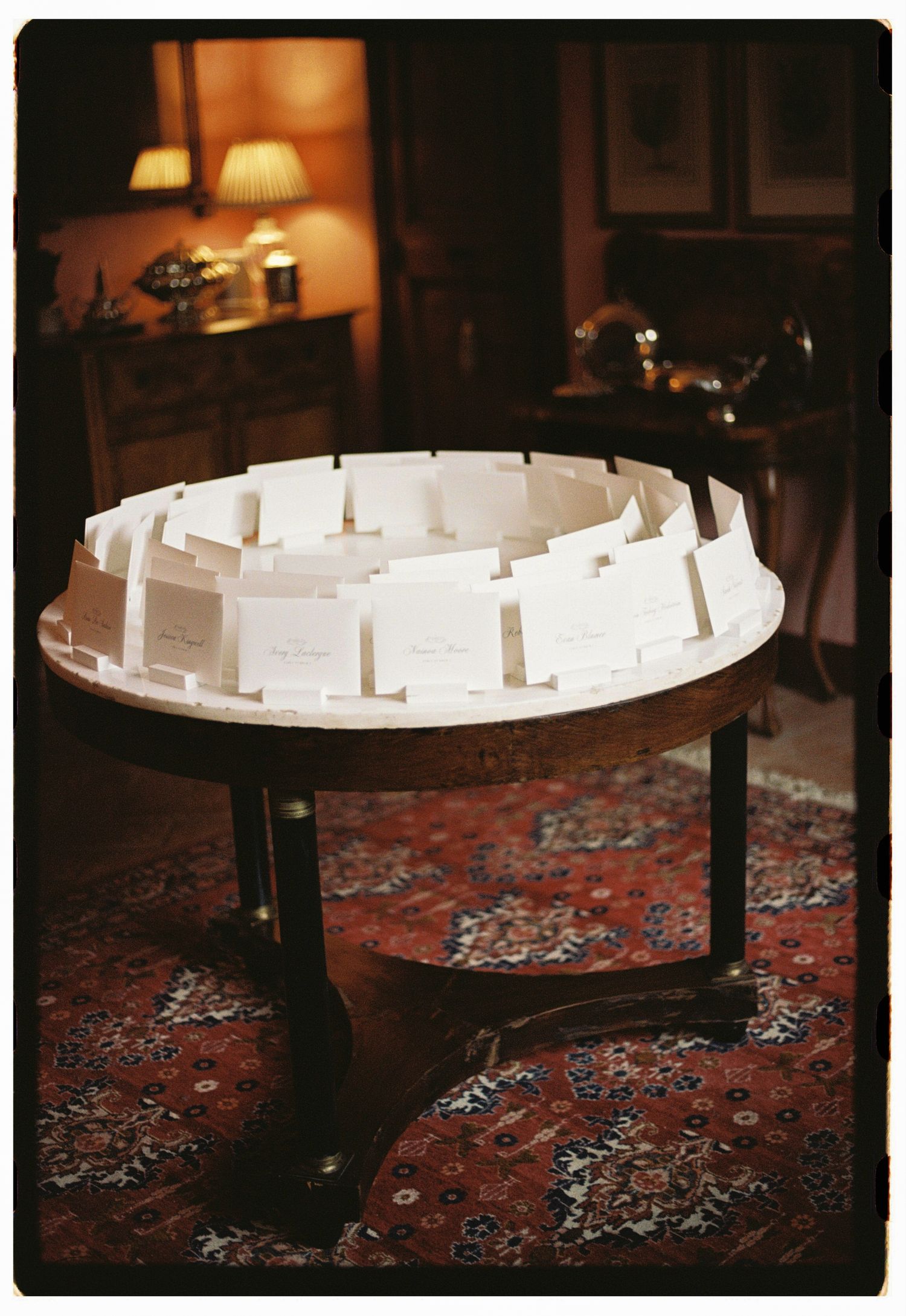 Circular wooden table displaying elegant white place cards arranged for a wedding reception seating chart.