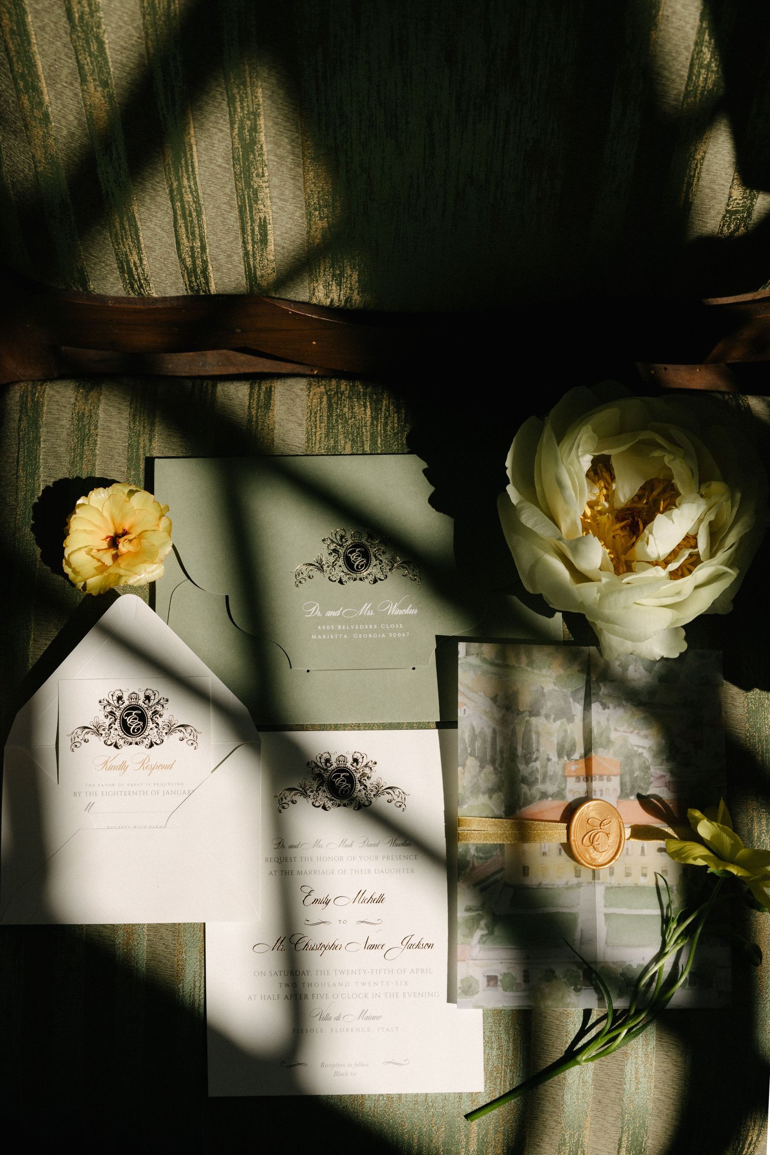 Elegant wedding invitation suite with sage green envelopes, wax seal, ribbon, and fresh white peony and yellow flowers.