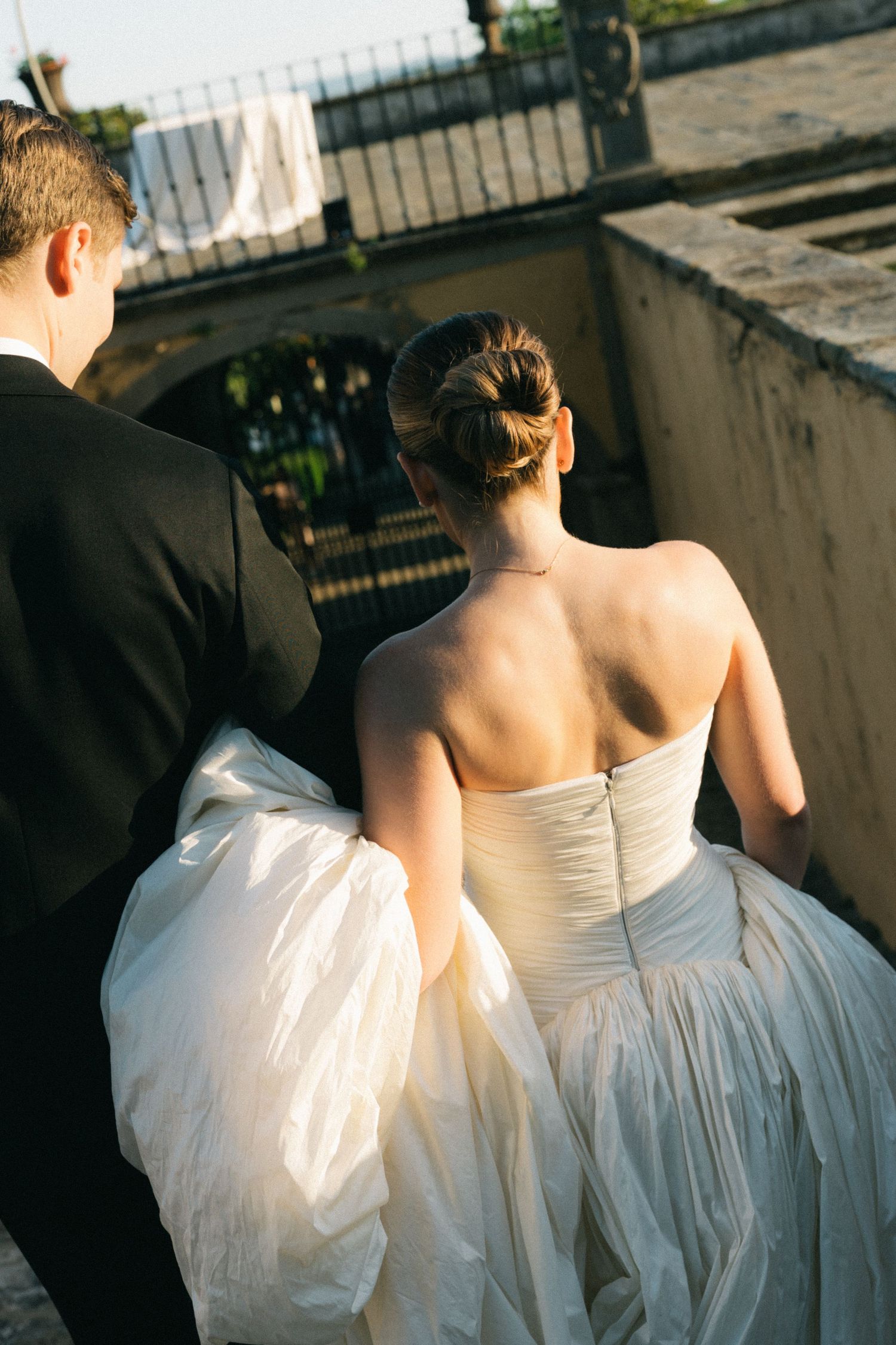 Bride in strapless white ball gown and groom in black tuxedo walking up stone steps together.